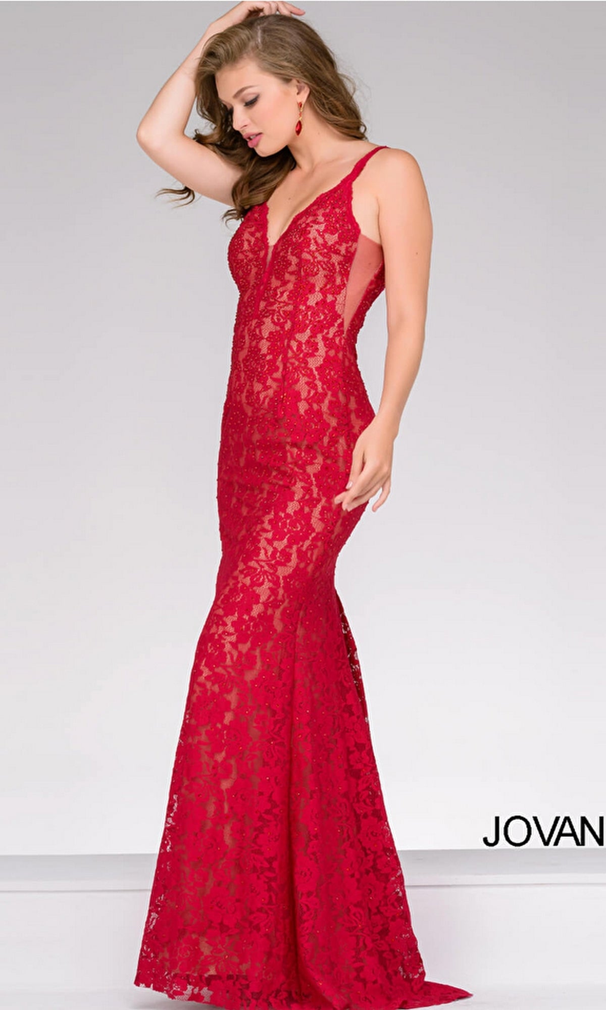 A woman models the red Illusion-Sides Long Lace Prom Dress (Jovani 48994), featuring a fitted bodice, flared floor-length skirt, open back, and sleeveless lace design. The plain light background shows “JOVAN” partially in the corner.