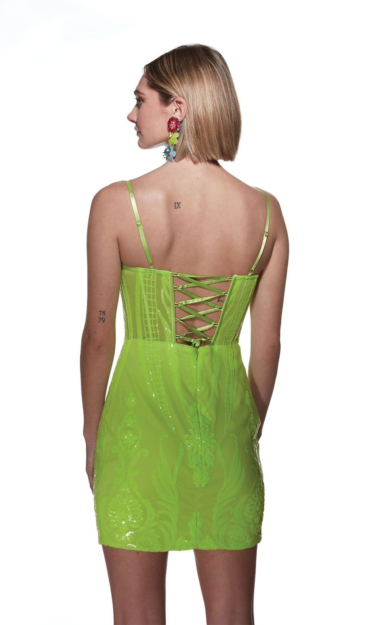 A person wearing the Alyce V-Neck Short Sequin-Print Hoco Dress 4901 in neon green, featuring spaghetti straps and lace-up back detailing, stands facing away from the camera against a white background.
