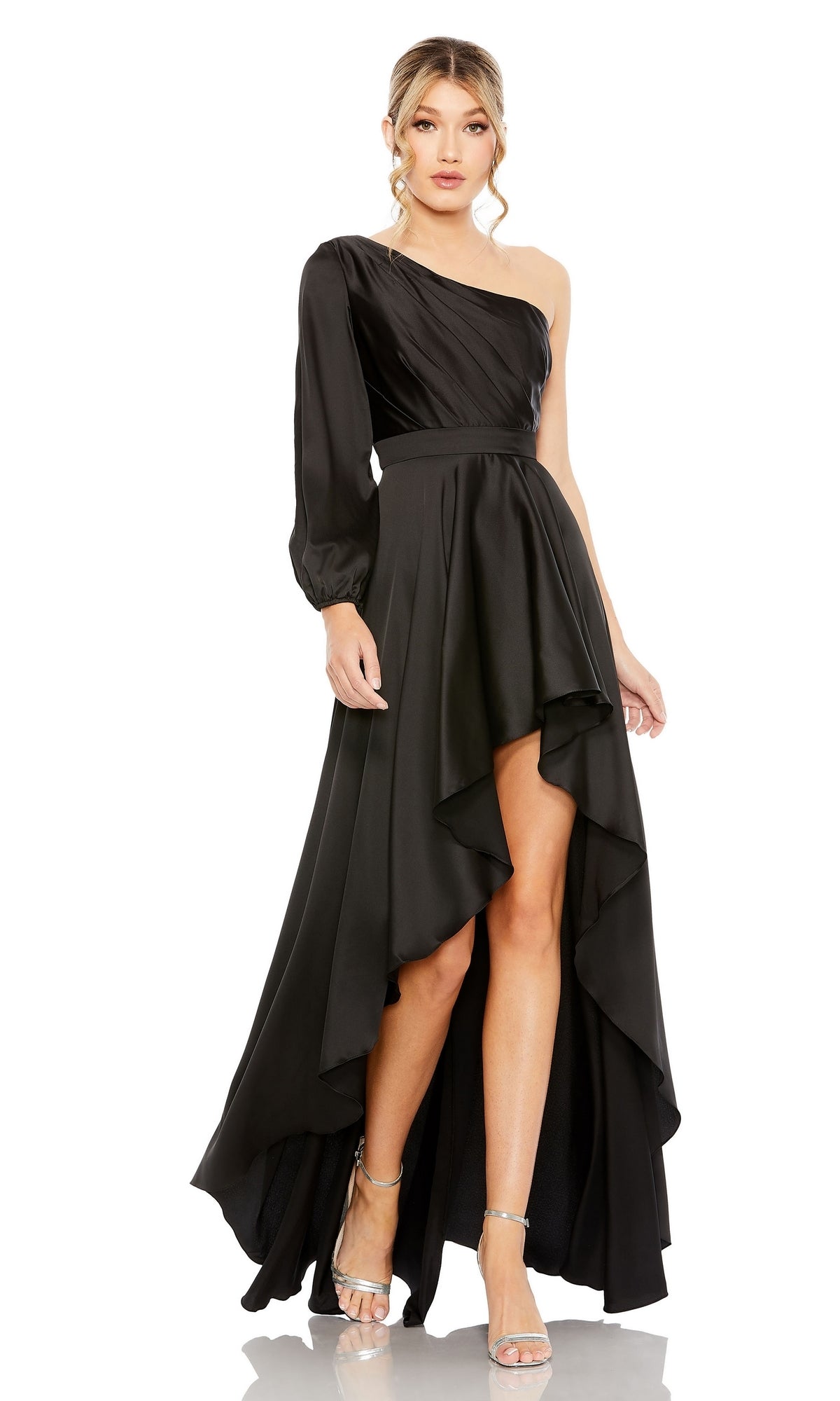 A woman wears the Mac Duggal 49141 One-Sleeve High-Low Prom Dress in black, featuring an asymmetrical hem and one long sleeve, paired with silver high-heeled sandals.
