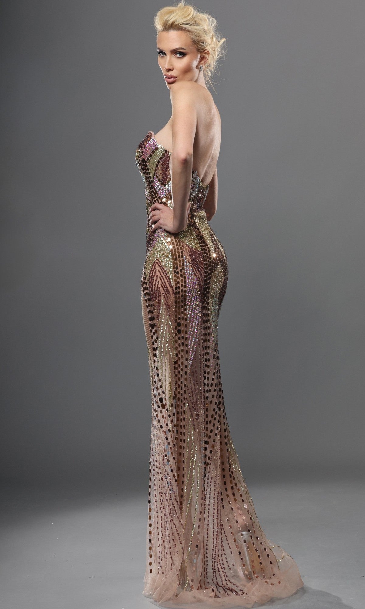 A woman stands sideways with one hand on her hip against a plain gray background, wearing the Long Formal Dress: Jovani 49201— a strapless, form-fitting designer gown adorned with sequin beaded embellishments.