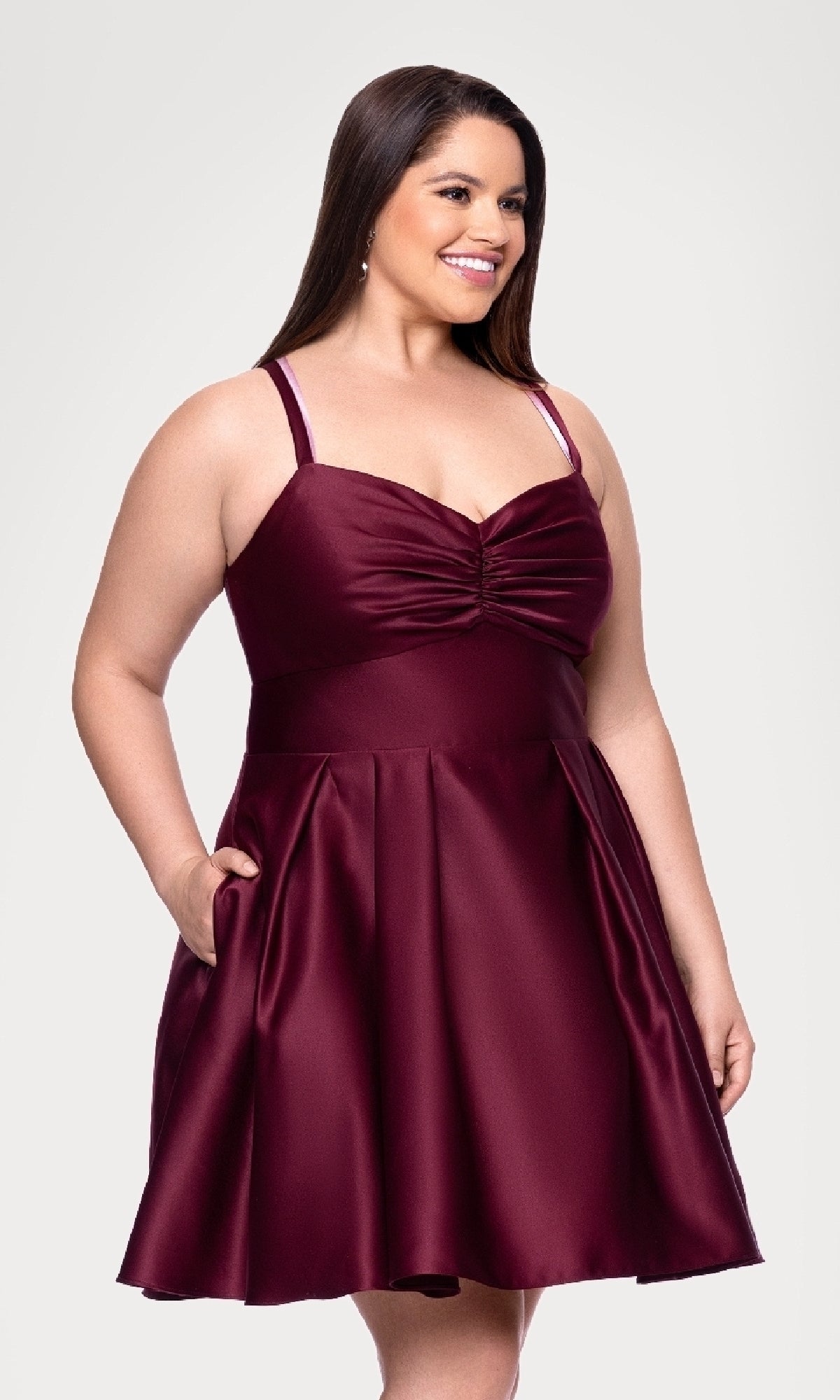 A woman is standing and smiling in the Blondie Nites 4927BNW Plus Short Wine Hoco Dress, featuring a sleeveless design, fitted bodice, and flared knee-length skirt.