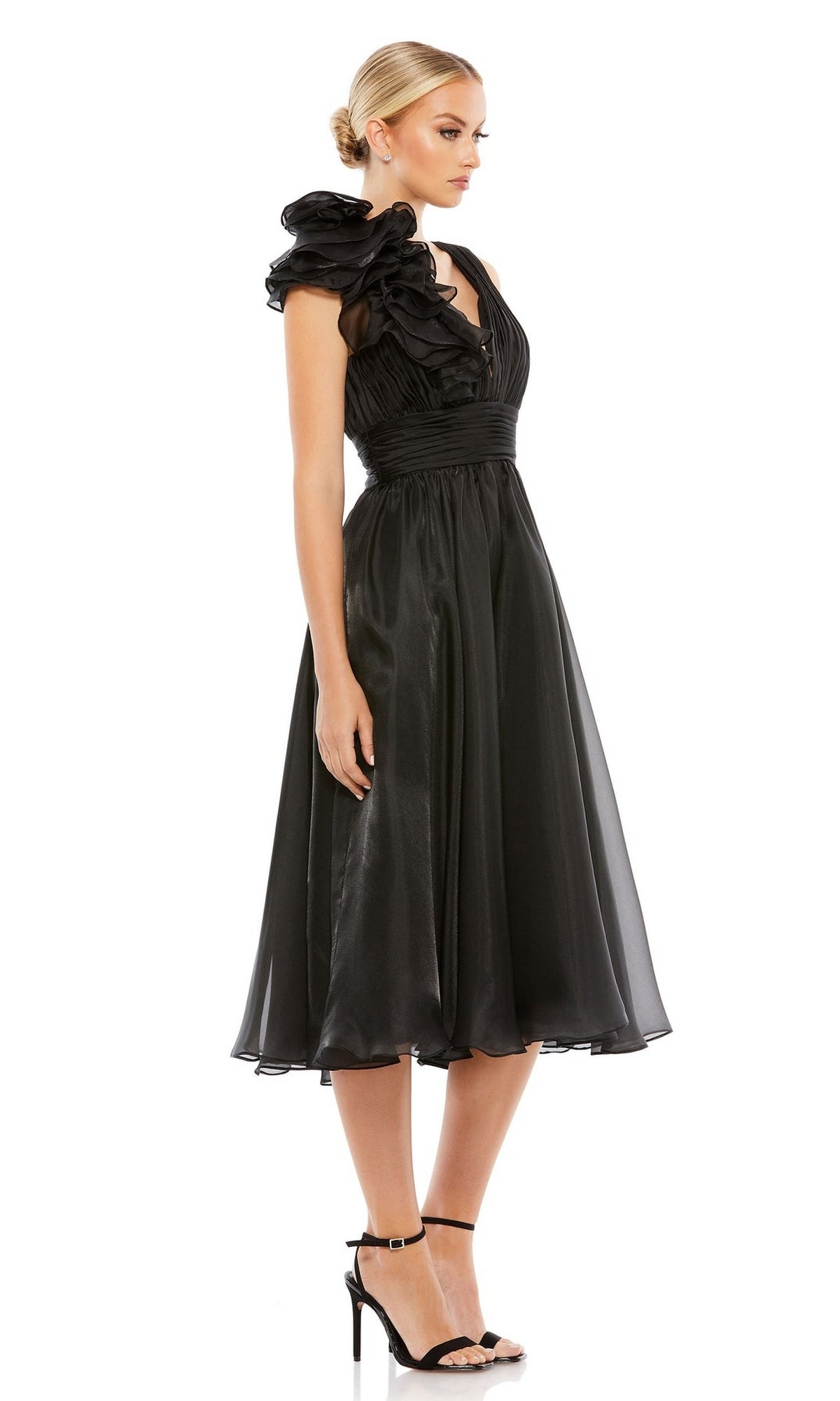 A woman models the Mac Duggal 49494 short ruched wedding-guest dress with black high-heeled sandals, posing against a white background.