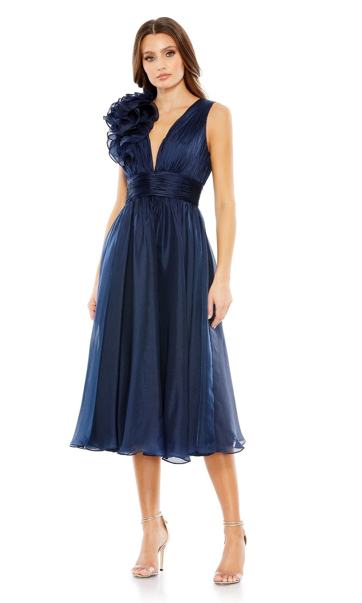 A woman wears the Mac Duggal 49494 short ruched wedding-guest dress—a navy blue, sleeveless, knee-length style with a deep V-neck, dramatic one-shoulder ruffle—paired with silver high-heeled sandals.