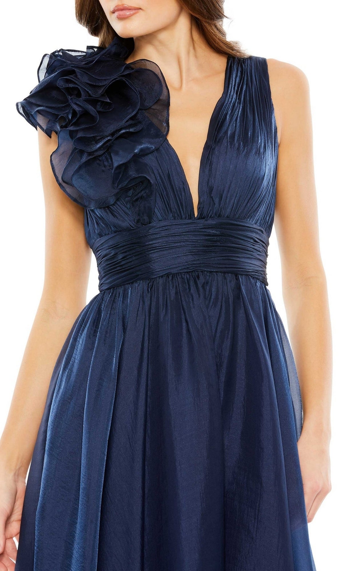 A woman wearing the Short Ruched Wedding-Guest Dress (Mac Duggal 49494), featuring a sleeveless deep blue design with a pleated bodice, ruched waistband, and a large ruffled detail on the left shoulder.