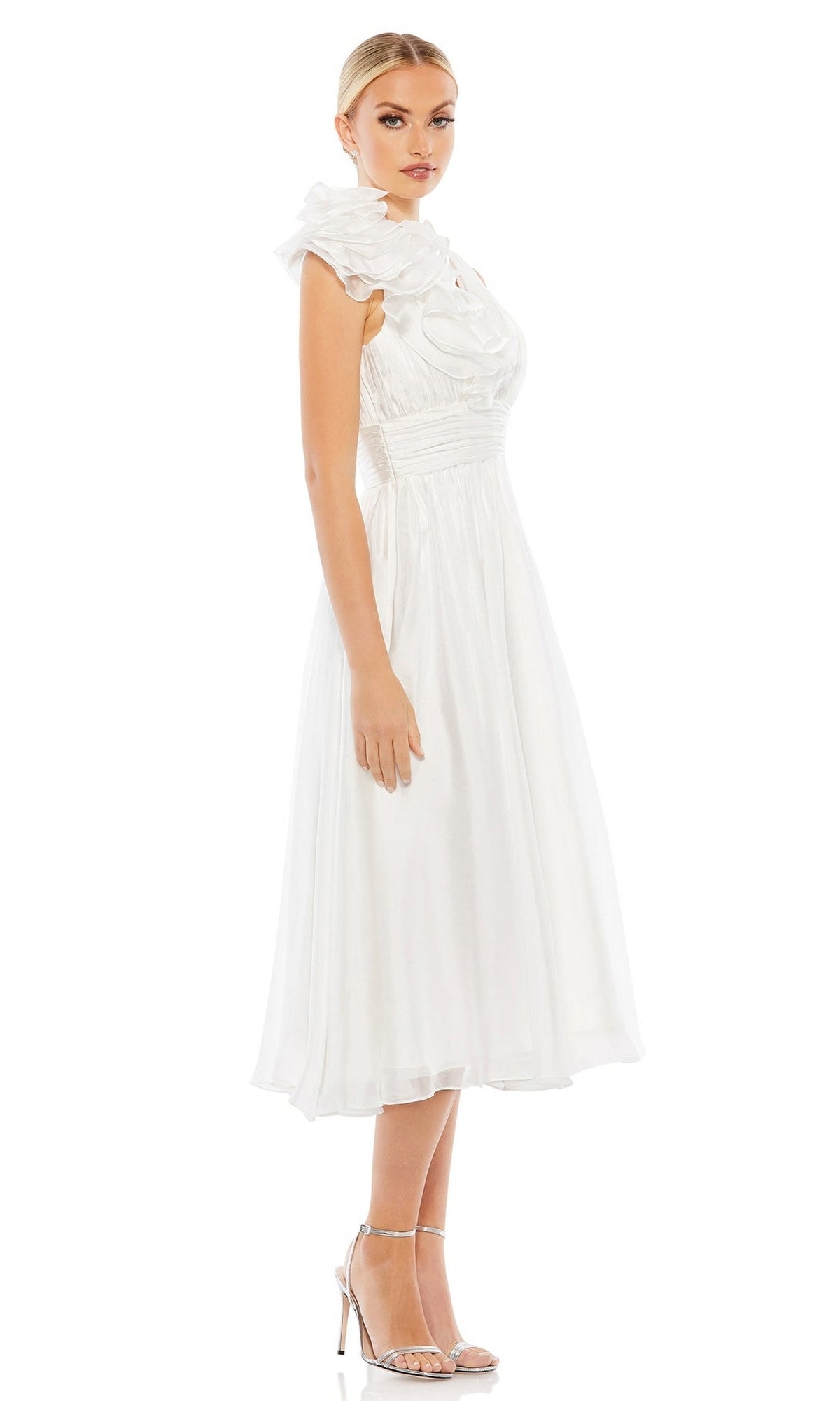 A woman stands in profile wearing the Mac Duggal 49494 Short Ruched Wedding-Guest Dress—sleeveless, white, midi-length with a ruffled high neckline—paired with silver high-heeled sandals against a plain white background.