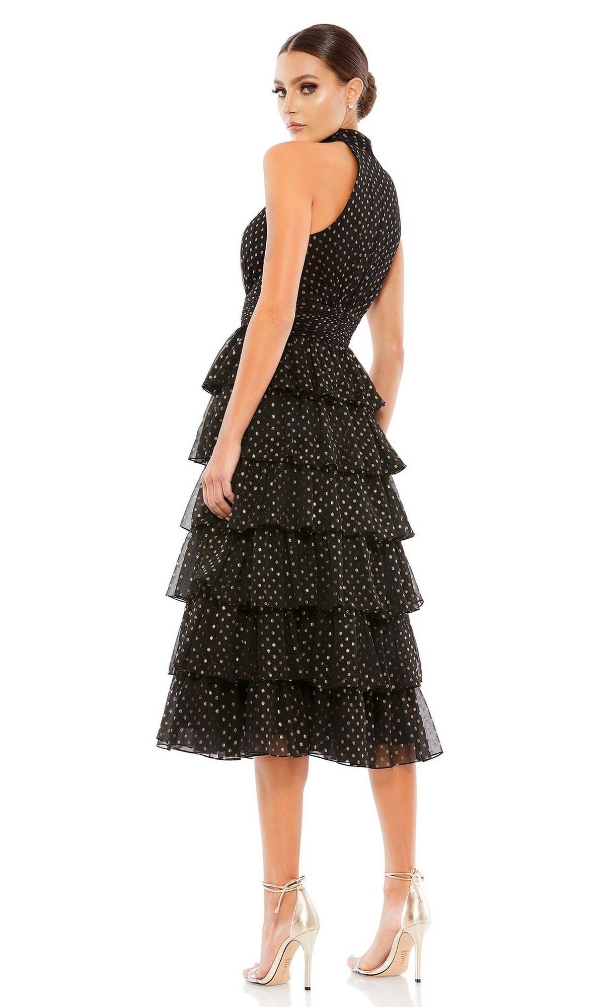 Woman in profile wears the Mac Duggal 49510 midi black wedding guest dress with gold polka dots and metallic high-heeled sandals, set against a white background.