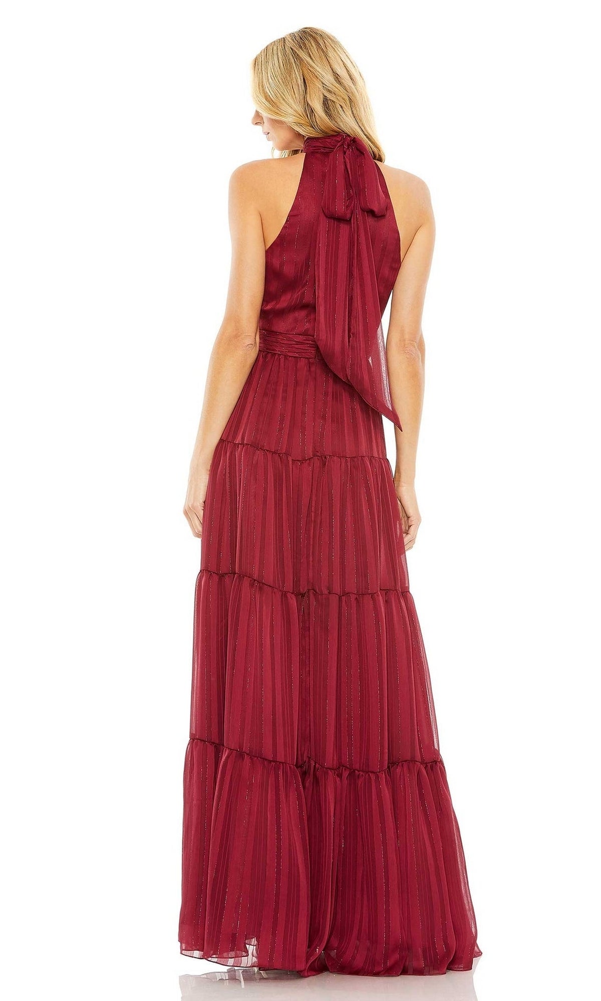 A woman stands facing away in a sleeveless, floor-length black Mac Duggal 49515 dress with tiered layers, a halter neckline, and bow detail at the back.