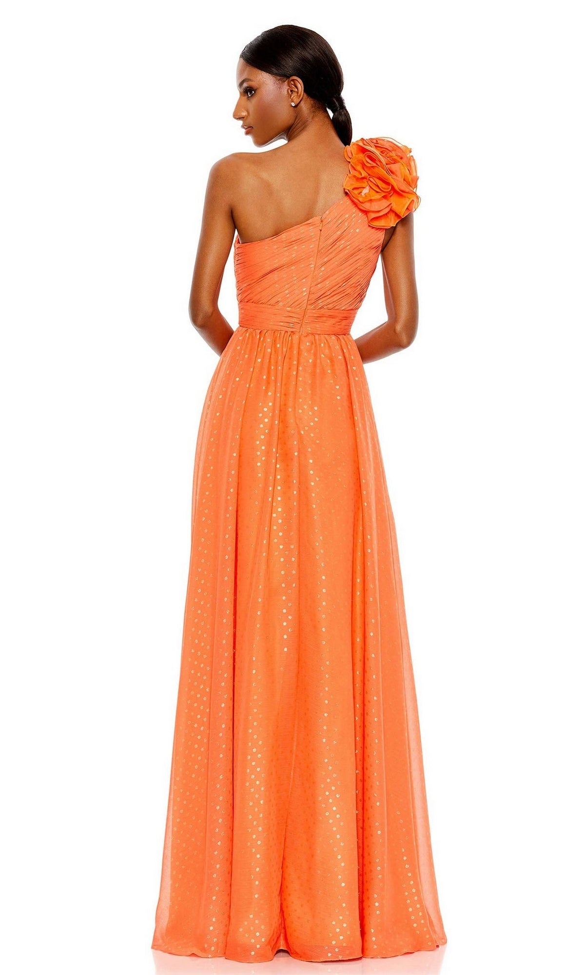 Woman poses with her back to the camera in the Mac Duggal 49536, a one-shoulder orange long formal dress featuring pleats, a large floral accent, and subtle polka dot patterns.