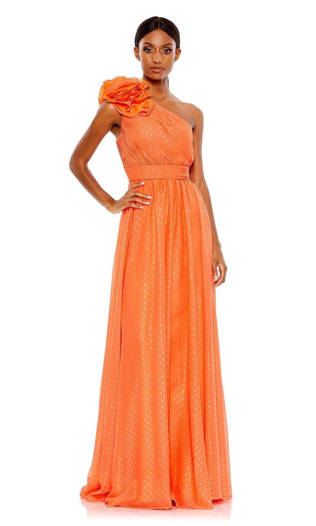 A woman stands wearing the Mac Duggal 49536, a floor-length orange one-shoulder formal dress with pleats, floral shoulder detail, and subtle dotted patterns.