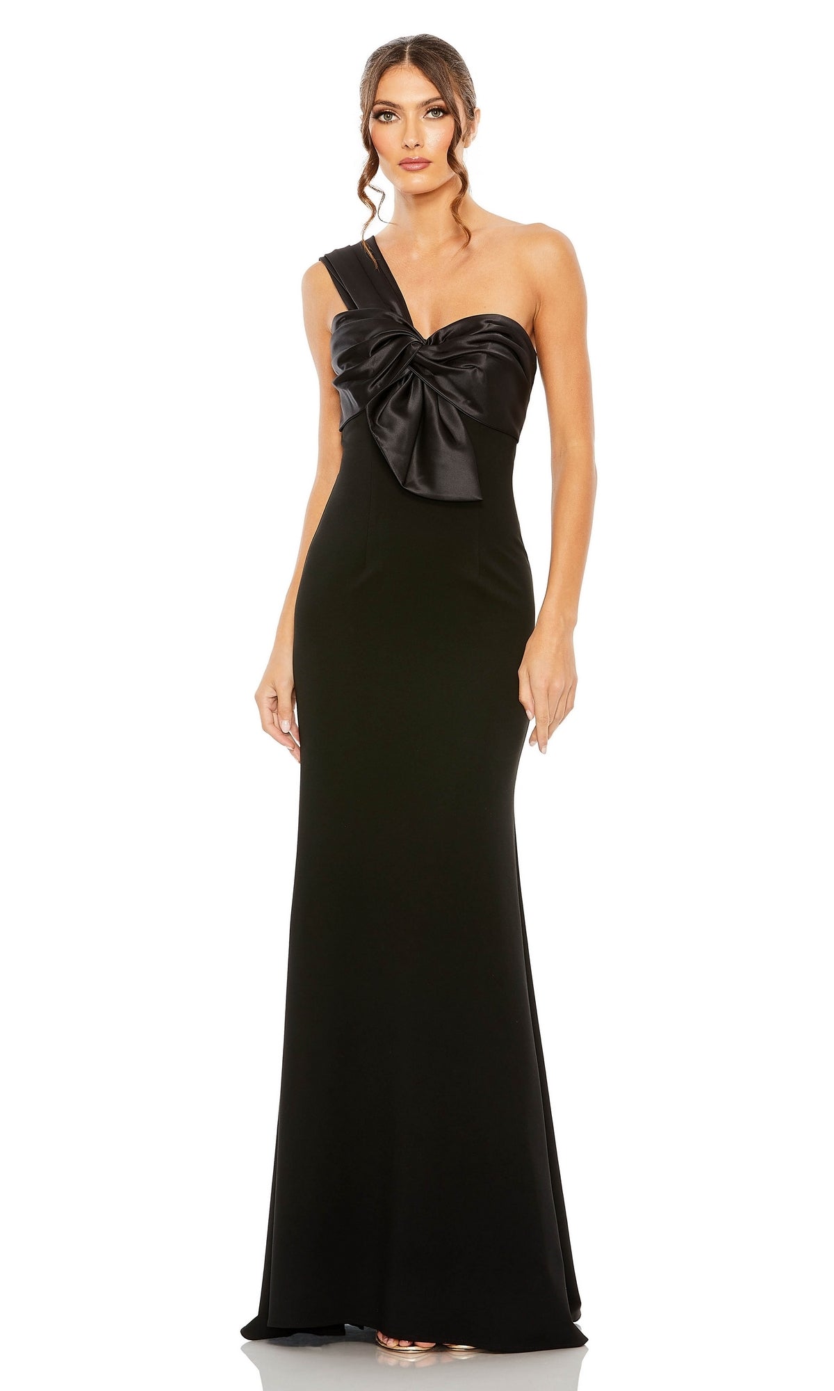 A woman wears the Mac Duggal One-Shoulder Long Bow Prom Dress 49547, a floor-length black evening gown featuring a dramatic satin bow on the bodice, exuding classic elegance.