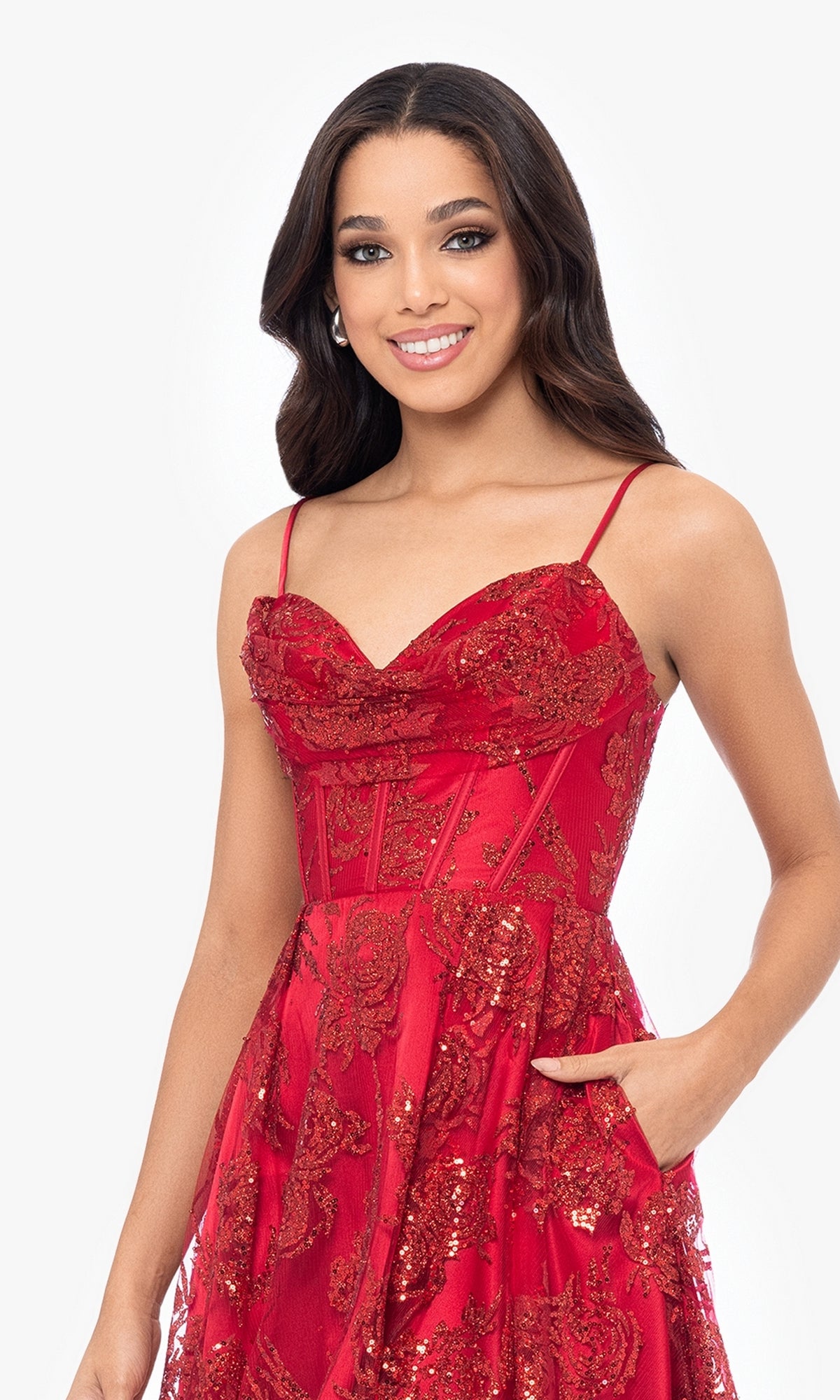 A woman wearing the Short Red Glitter Homecoming Dress 4960BN, featuring sequins and thin straps, smiles at the camera against a white background.