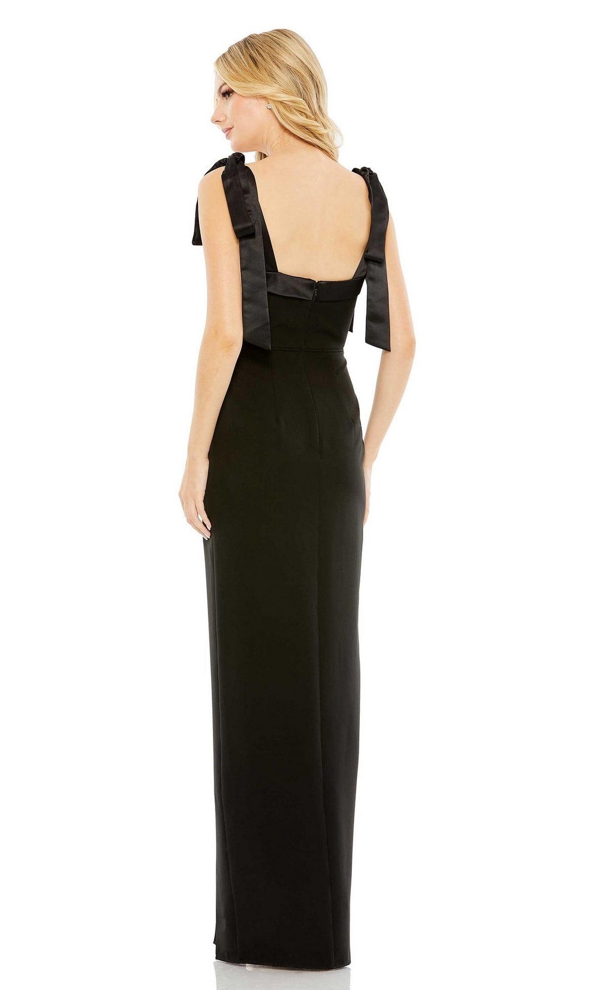 A woman stands facing away, wearing the Mac Duggal 49620 Tie-Strap Long Black Formal Dress—a classic sleeveless gown with tie straps and a floor-length skirt, perfect for formal occasions.