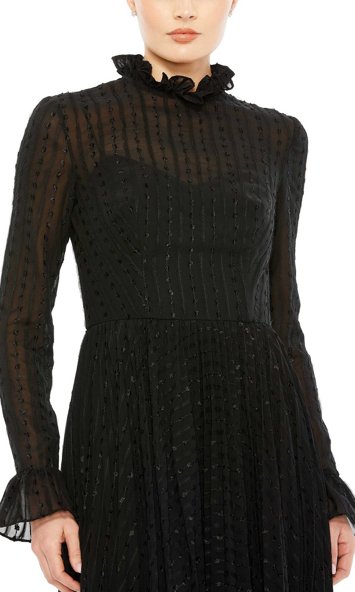 Person wearing the Short Wedding Guest Dress 49627 by Mac Duggal, featuring black sheer long sleeves, a ruffled high neck, and subtle vertical dotted pattern with a pleated knee-length style. The person’s face is partially visible.