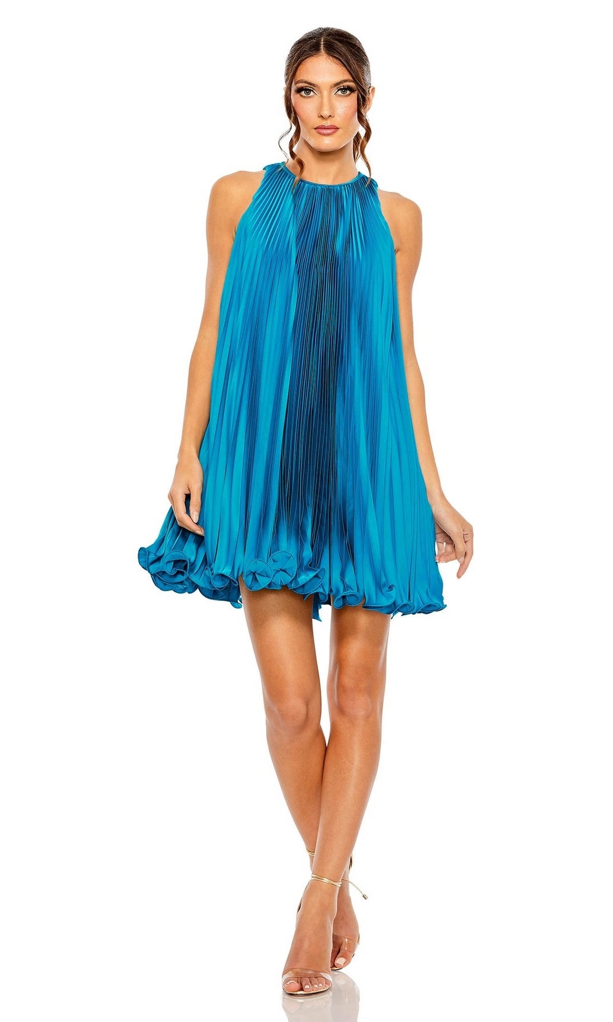 A woman in the Mac Duggal 49636 short pleated semi-formal dress and strappy heels stands against a white background.
