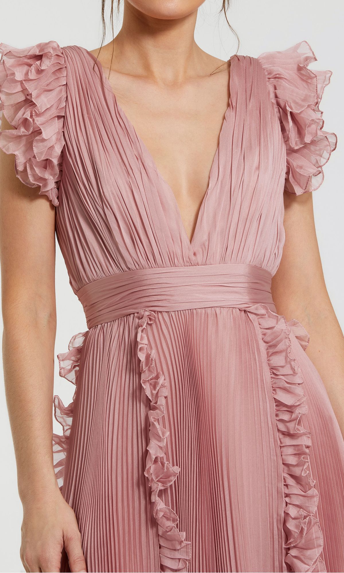 A person wearing the Short Wedding Guest Dress 49675 by Mac Duggal in rose pink chiffon, featuring pleated details, ruffle cap sleeves, and a deep V-neckline.