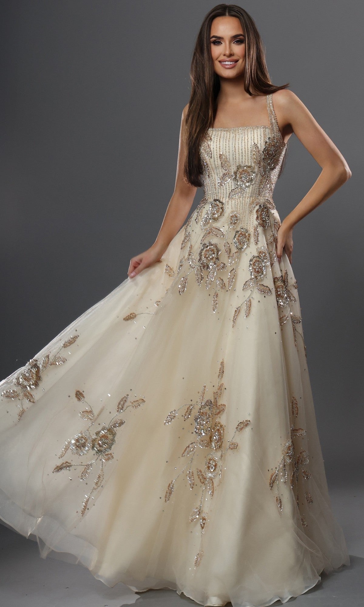 A woman poses against a gray background wearing the Long Formal Dress: Jovani 49697 in champagne, a floor-length gown featuring floral sequin embellishments and a square neckline, exuding elegant style.