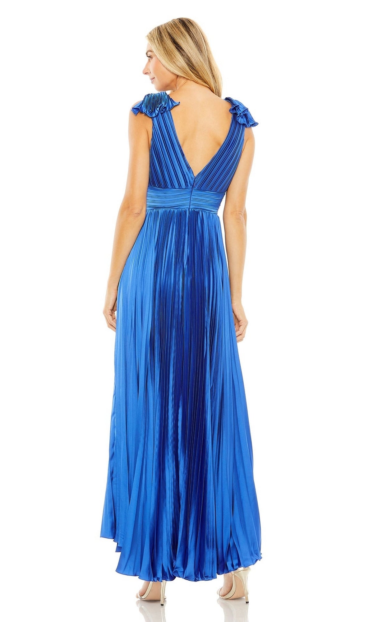 A woman in the Mac Duggal 49734 pleated tea-length formal dress in metallic blue, with cap sleeves and a deep V-back, stands on high heels and is viewed from behind.