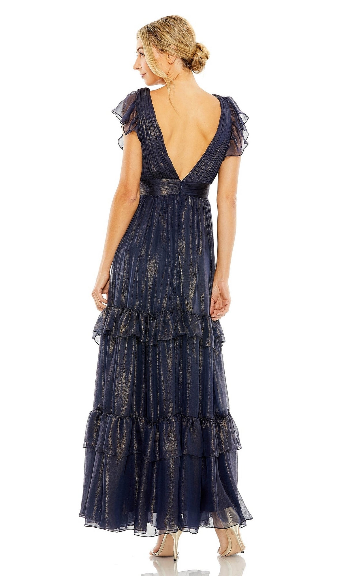 A woman stands facing away, wearing the Mac Duggal Long Formal Dress 49742—a floor-length, midnight blue gown with ruffle details, flutter sleeves, a deep V-back, and shimmering fabric.
