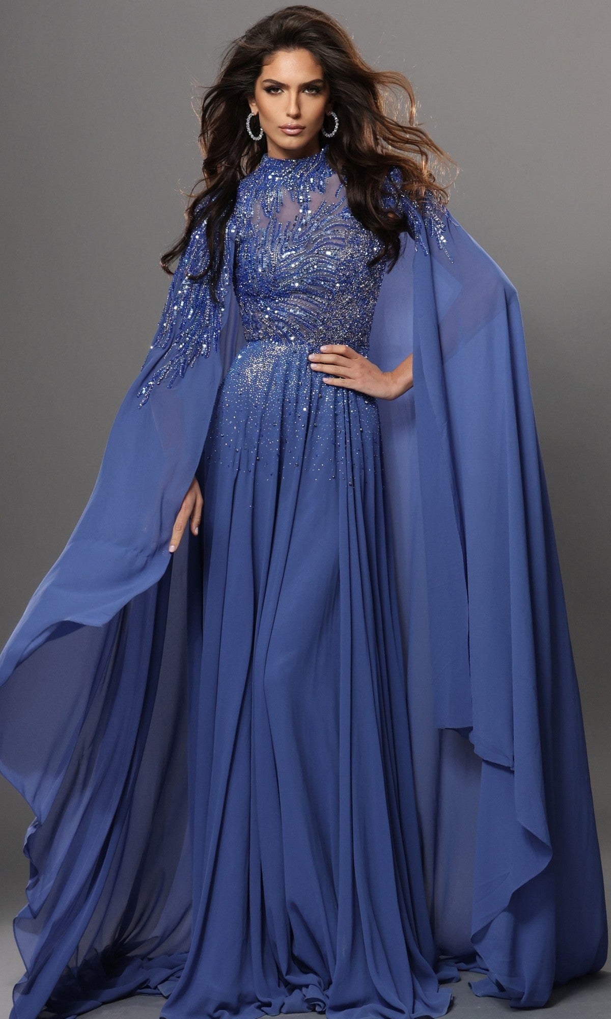 A woman wearing the Jovani 49742 long formal dress in royal blue, featuring beaded details, embellished cape sleeves, and long chiffon fabric, poses against a neutral background—an ideal choice for an elegant mother-of-the-bride ensemble.
