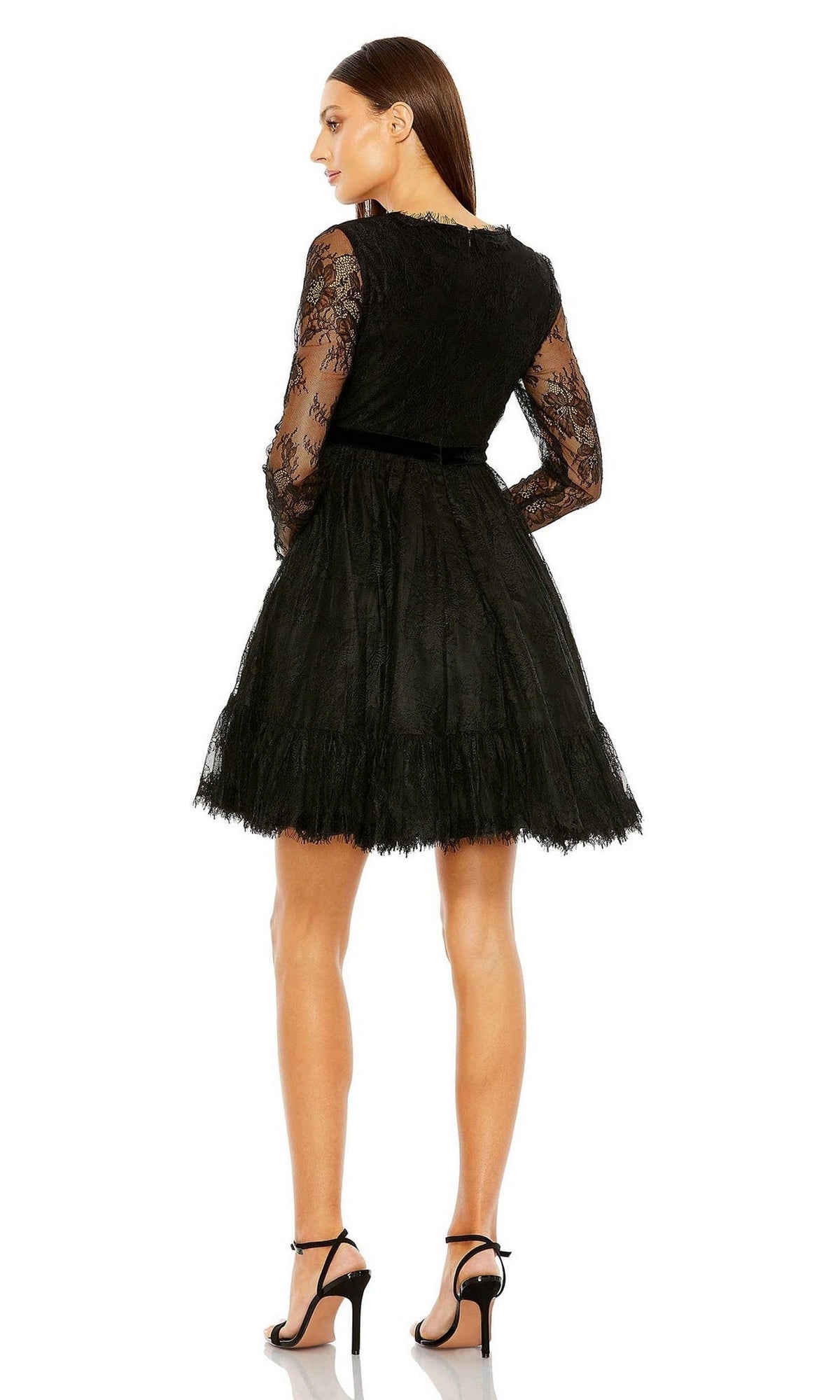 A woman stands facing away, wearing the Mac Duggal 49794 short black wedding guest dress with long sleeves and a flared skirt, paired with black high-heeled sandals.