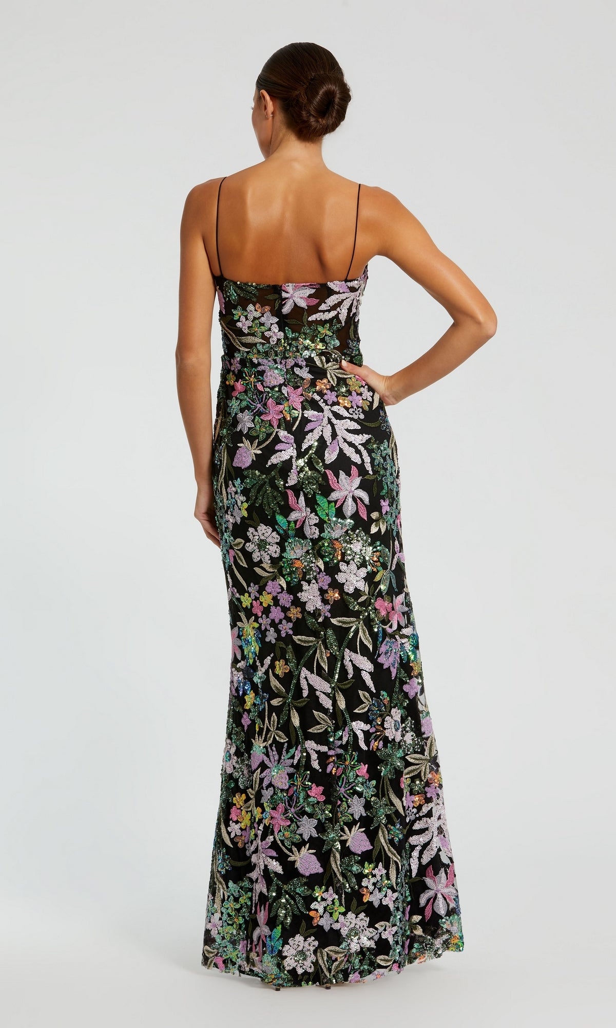 Woman stands with her back to the camera, wearing the Mac Duggal 49827 Sequin-Print Black Formal Dress—an elegant long gown featuring colorful floral embroidery and delicate thin straps.
