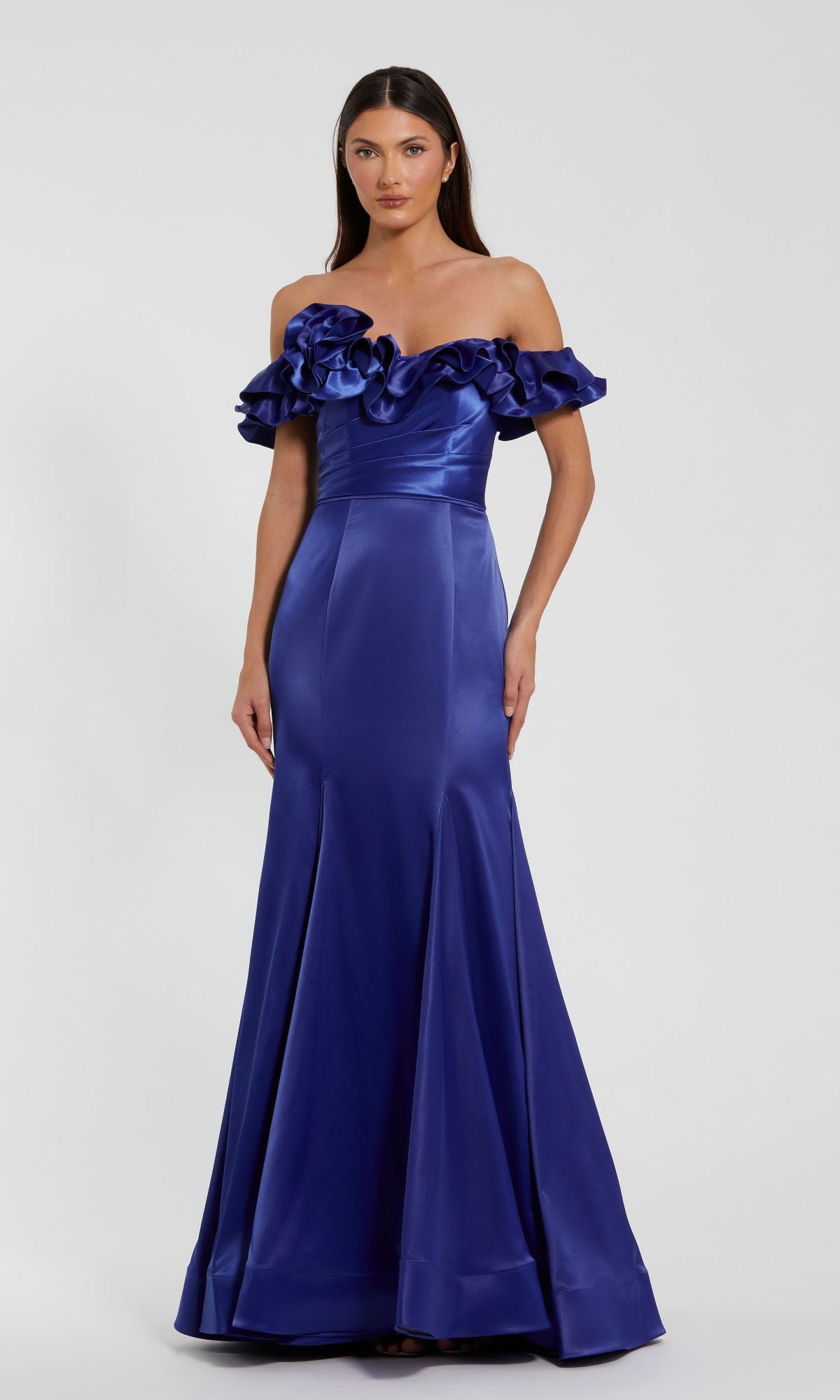 A woman stands against a plain background, wearing the Mac Duggal 49834 Ruffled Long Satin Prom Dress—an off-the-shoulder, royal blue gown with a floor-length skirt and ruffled neckline.