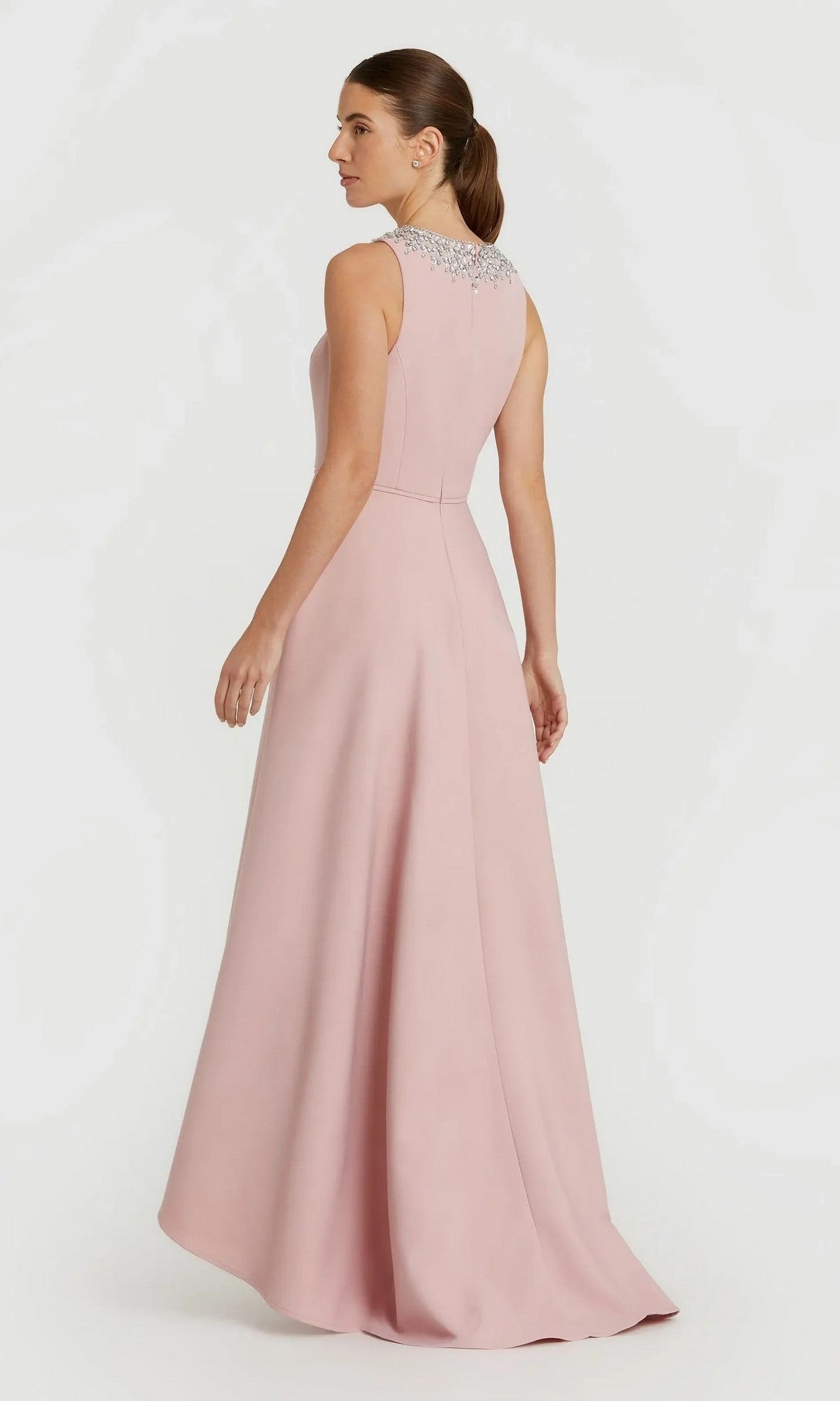 A woman in the Mac Duggal 49844 high-low formal dress, featuring a light pink sleeveless design with an embellished neckline and an elegant A-line skirt, stands against a plain white background.