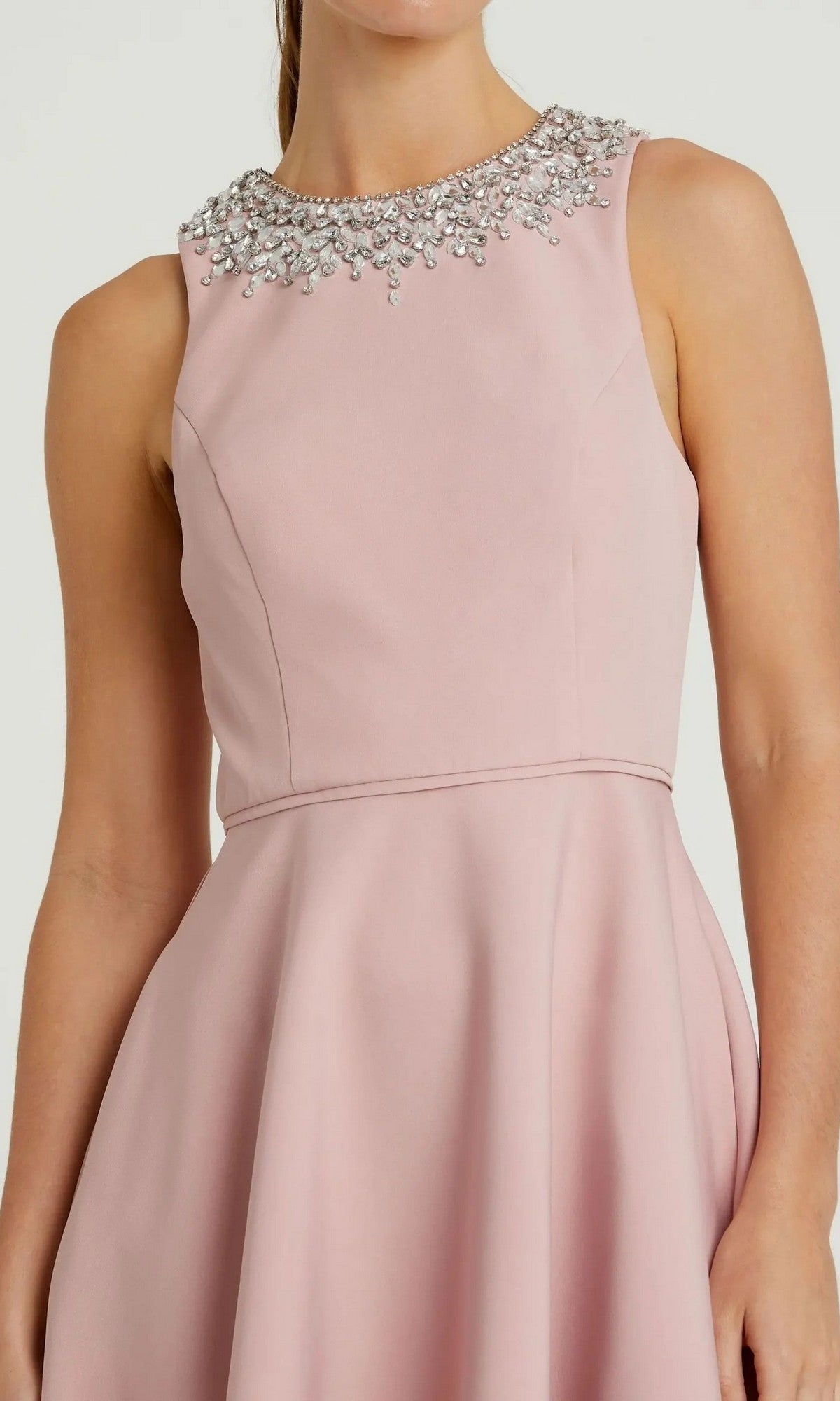 A woman wears the Mac Duggal 49844 High-Low Formal Dress, a sleeveless light pink gown with an A-line skirt, fitted waist, and jeweled neckline details.