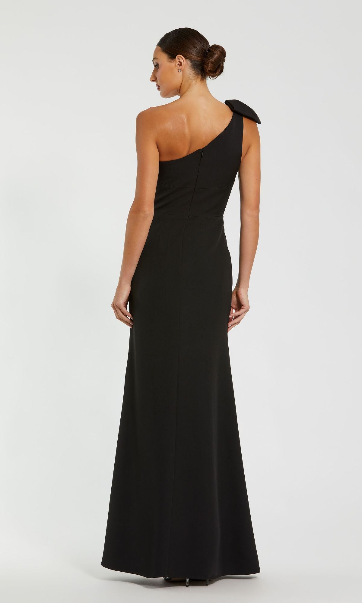 A woman models the Mac Duggal 49862 one-shoulder long formal dress with a shoulder bow, shown from the back against a plain background. This gown radiates timeless elegance.
