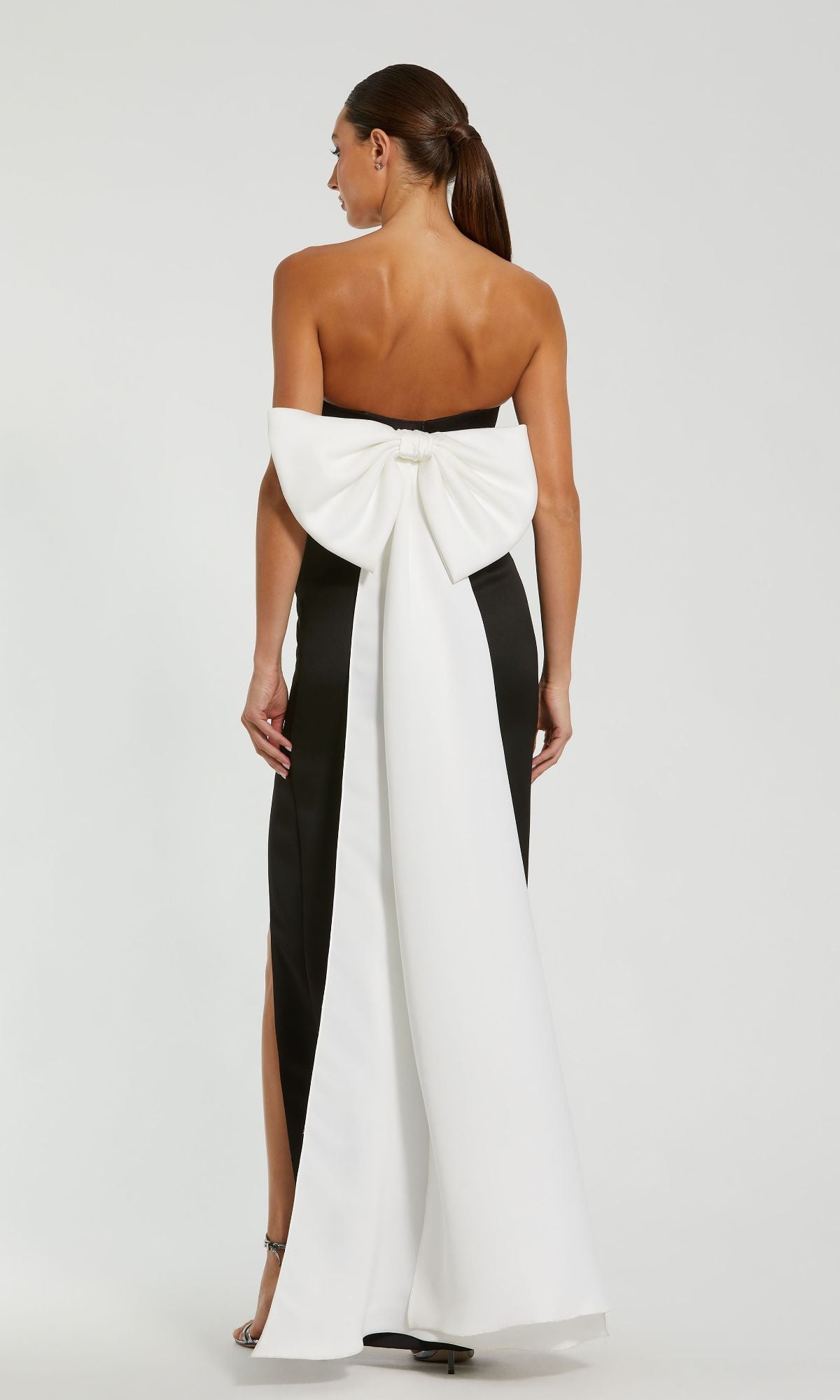 Woman in the Strapless Long Bow Prom Dress by Mac Duggal 49879, shown from the back, featuring a large white bow and a white panel running down the length of this elegant black and white evening gown.