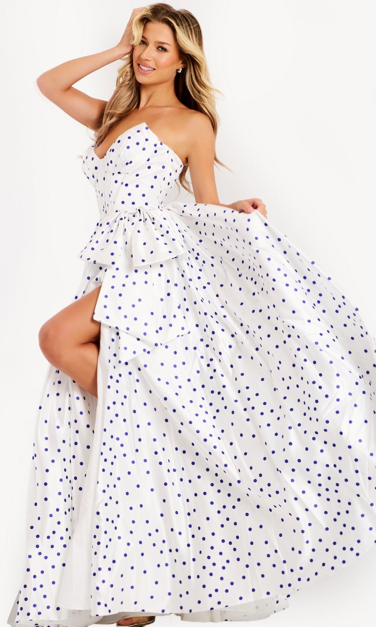 A woman poses in the Jovani 49899 Long Prom Dress in Off White/Royal, featuring a strapless polka dot design with a layered ruffle bodice, high slit, and voluminous satin A-line skirt—a playful twist on a classic look.