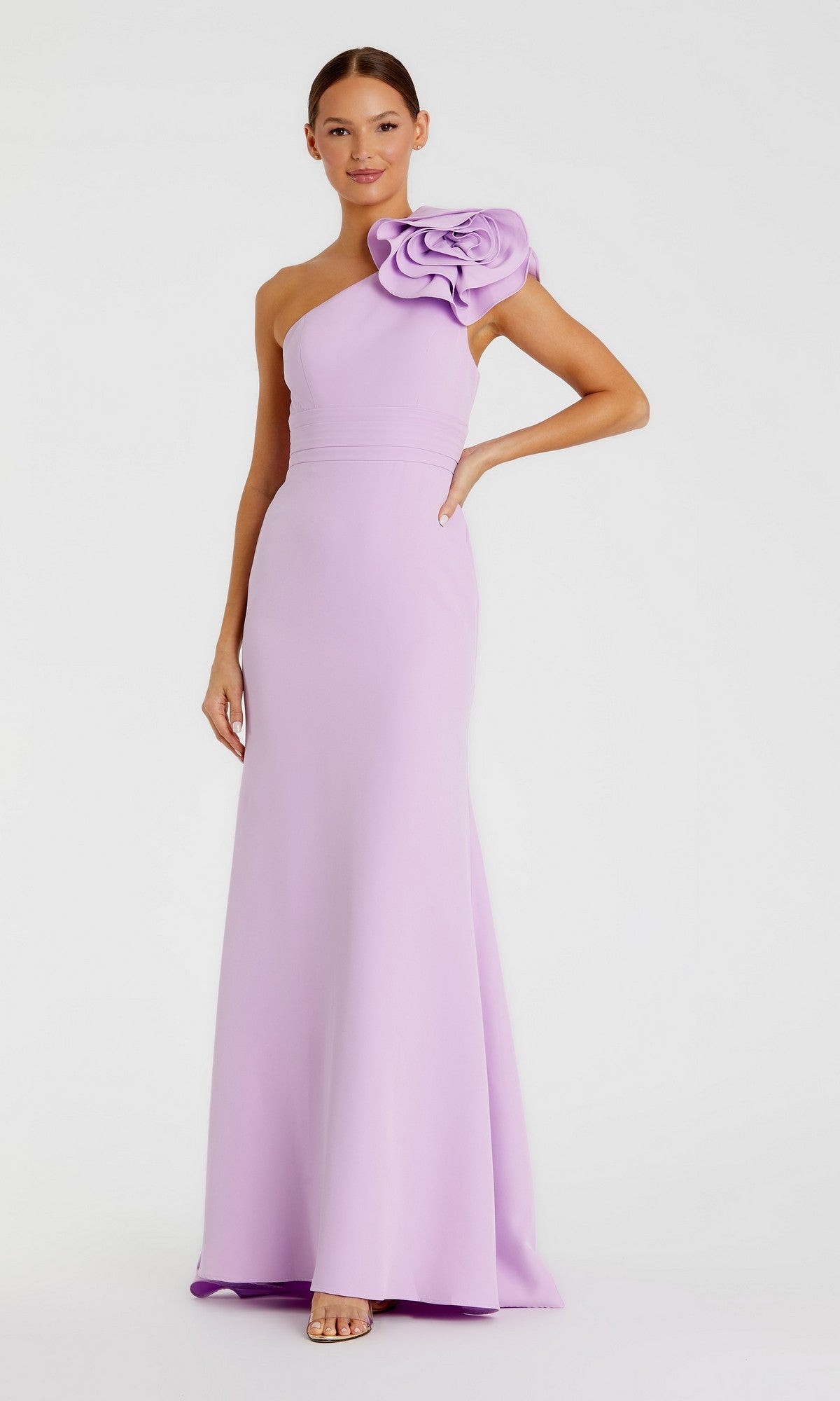 A woman stands wearing the Long Formal Dress: Mac Duggal 49966, a floor-length, one-shoulder gown in lilac with a prominent floral shoulder detail. This elegant crepe dress beautifully combines modern style with timeless sophistication.