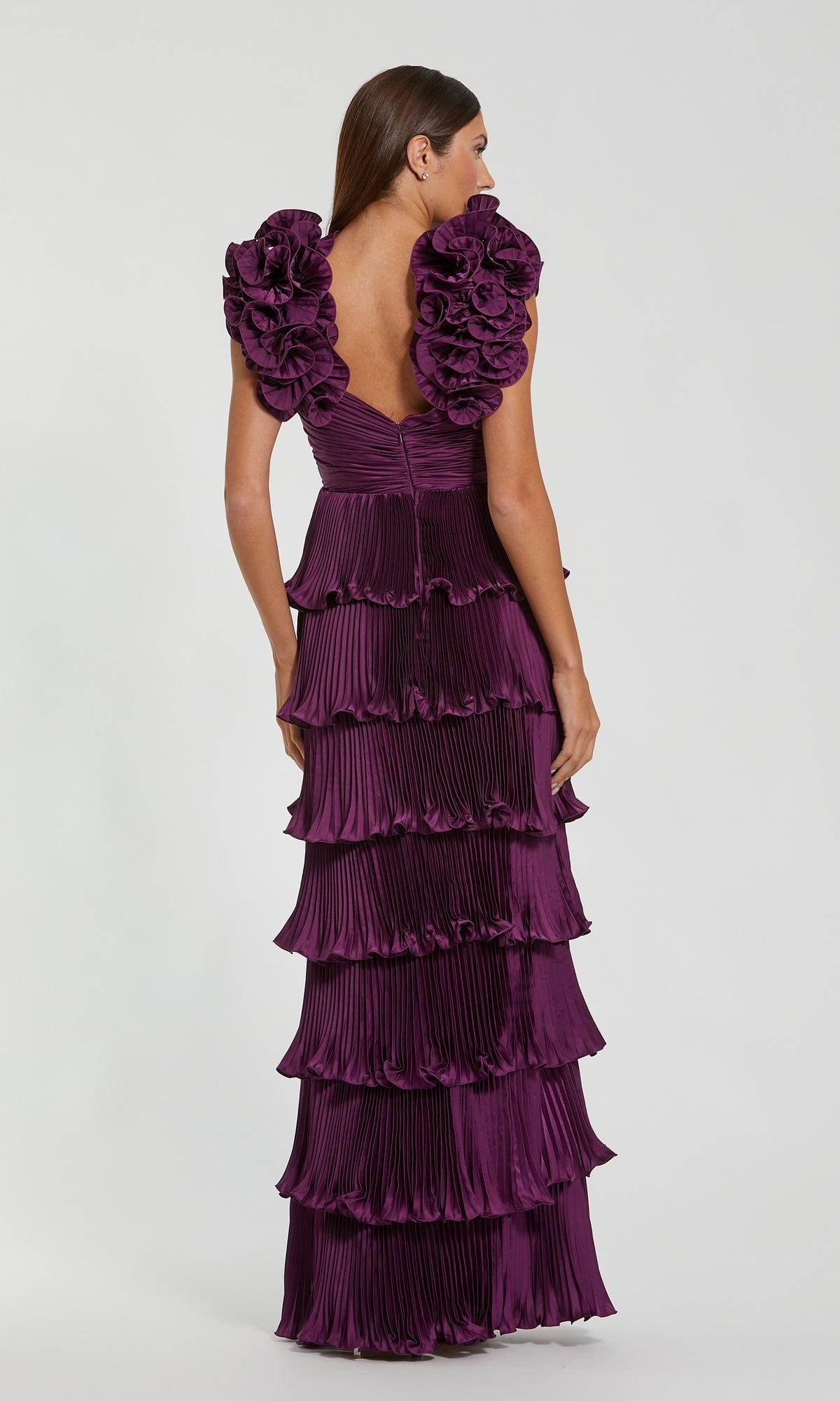 A woman is seen from the back against a plain white background wearing the Mac Duggal 49983 Long Formal Dress—a floor-length, dark purple gown featuring ruffle-tiered layers, pleated details, and ruffled shoulder accents.