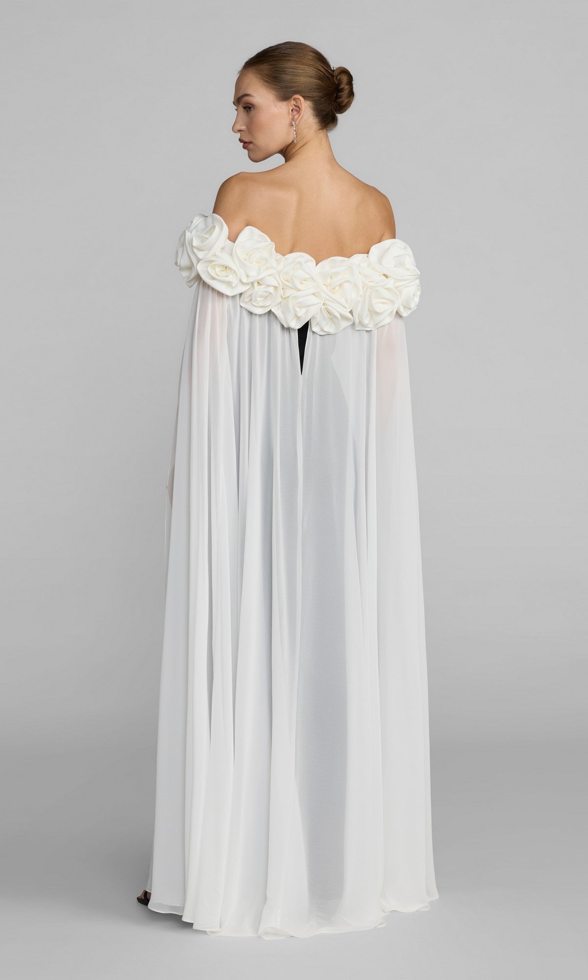 Woman wearing the Mac Duggal 50041 long formal dress, an off-the-shoulder crepe gown decorated with large fabric flowers along the neckline, standing against a plain background and facing away.