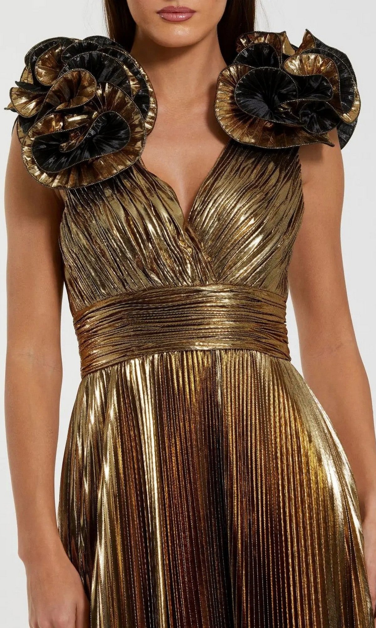 A woman wears the Mac Duggal 50084 long formal dress, a pleated sleeveless metallic gold gown featuring large ruffled black and gold floral shoulder accents.