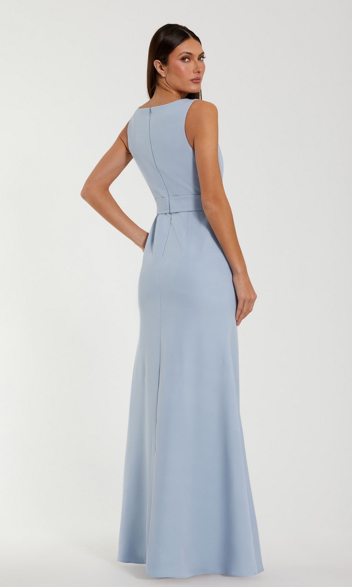 A woman stands facing away against a plain background, her head turned toward the camera, modeling the Mac Duggal 50097 Long Formal Dress—a sleeveless, floor-length crepe gown in light blue.