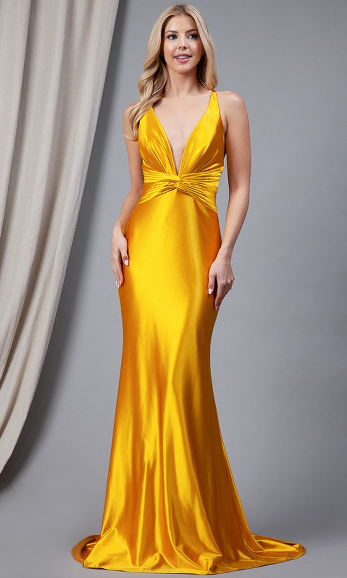 A woman poses before a gray backdrop wearing the Twist-Waist Deep V-Neck Long Prom Dress 5039—a sleeveless, floor-length yellow satin gown with a plunging V-neck and gathered waist detail.