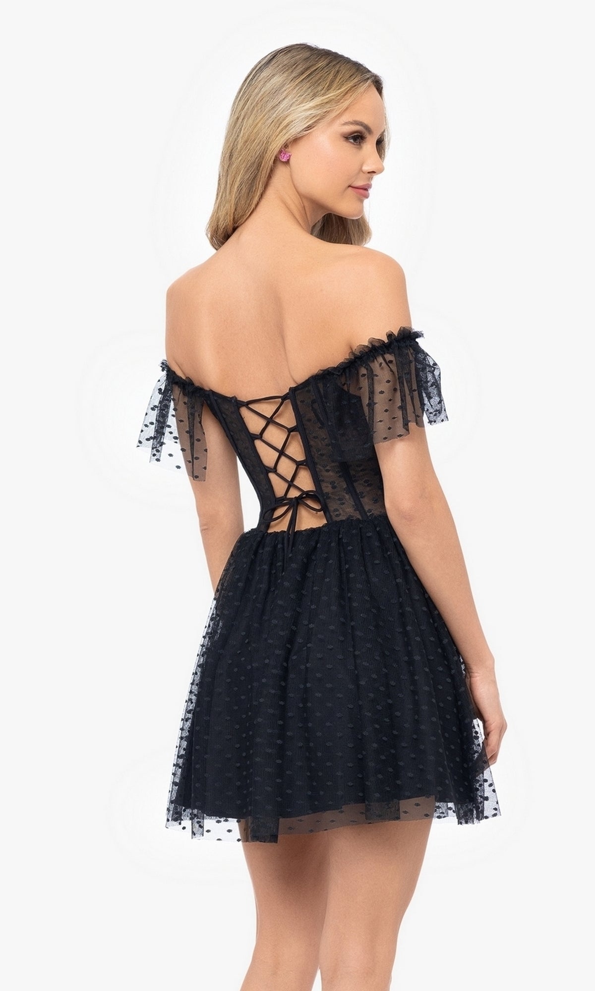 A woman models the Off-Shoulder Short Black Homecoming Dress 5054BN, featuring a lace-up back and sheer dotted sleeves—an affordable cocktail dress ideal for any special occasion.