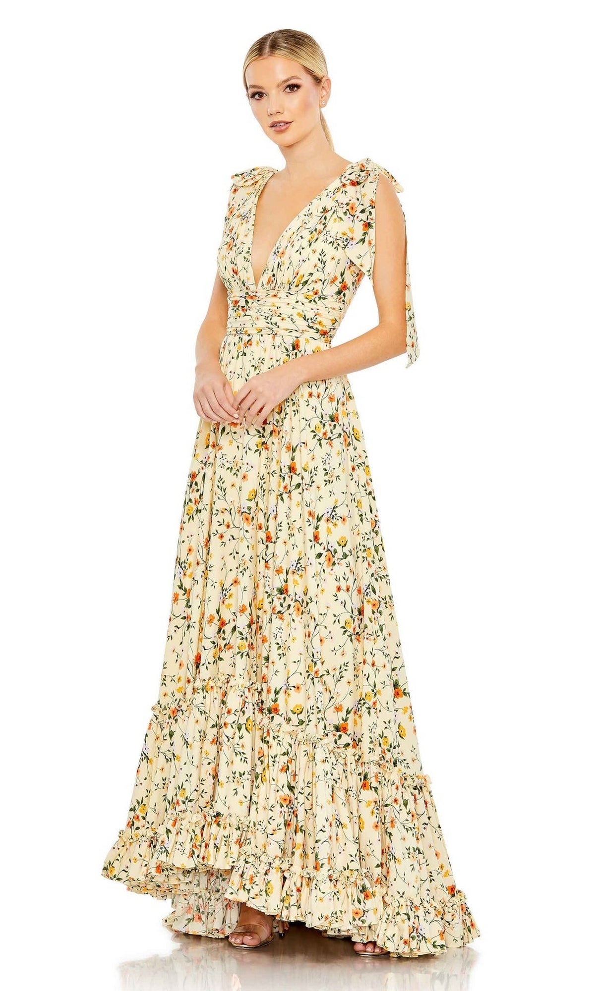 A woman wears the Long Formal Dress 50657 by Mac Duggal, a sleeveless, floral print A-line dress featuring a V-neck and ruffled hem, standing against a white background.