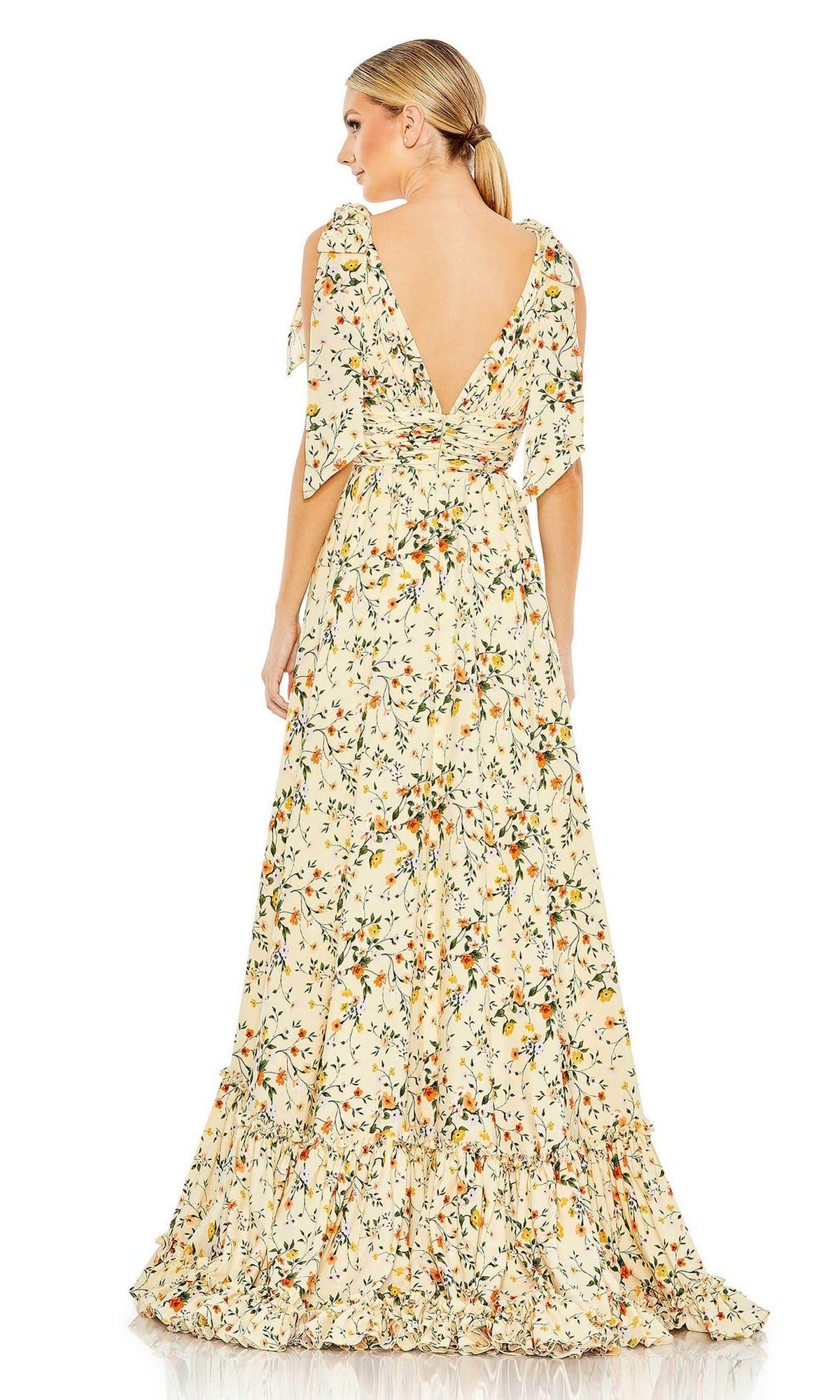 A woman faces away from the camera in the Long Formal Dress 50657 by Mac Duggal, featuring a cream floral print, deep V-back, and ruffled hem.