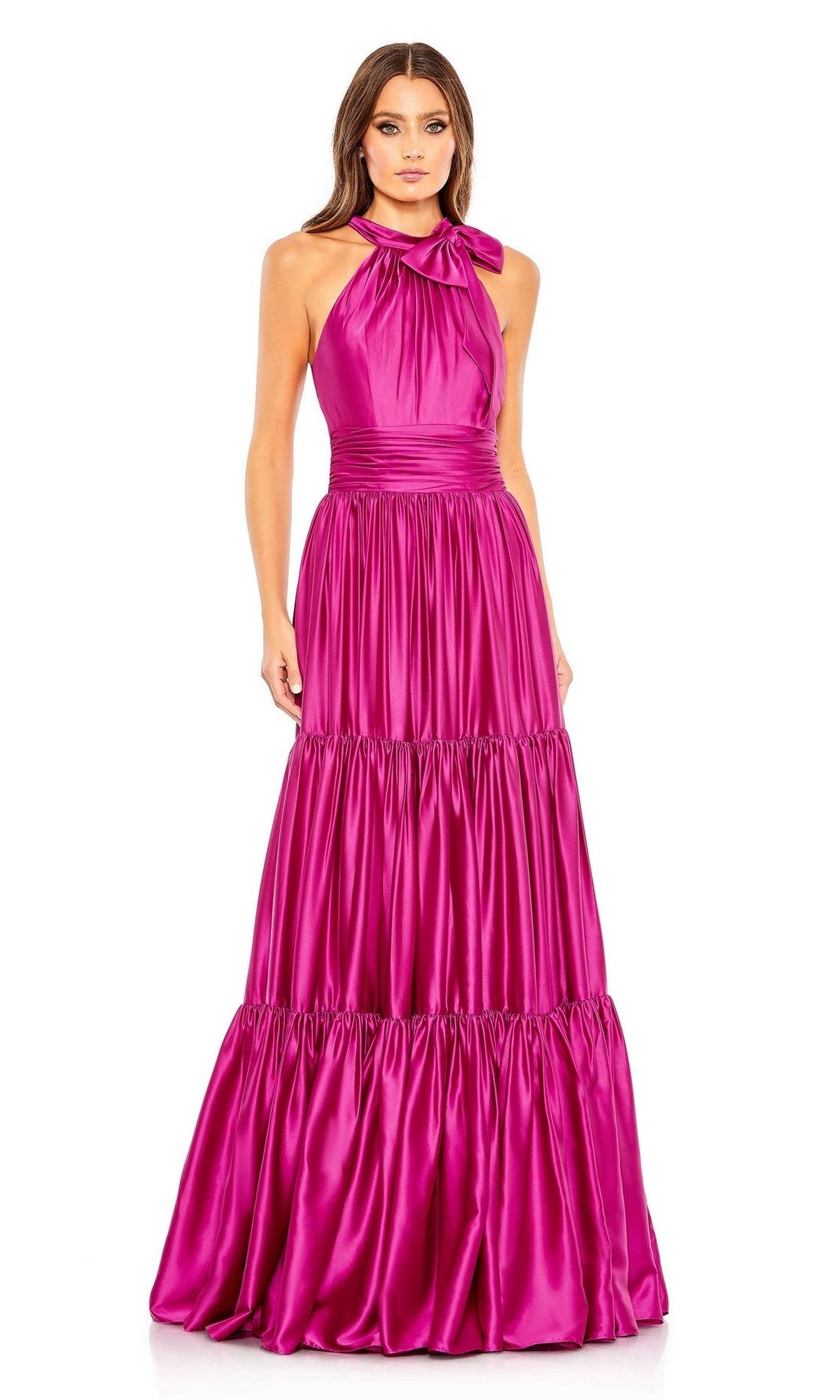 A woman wears the Mac Duggal High-Neck Satin Formal Dress 506581, a magenta floor-length A-line satin gown with a bow neckline and tiered ruffled skirt, standing against a plain white background.