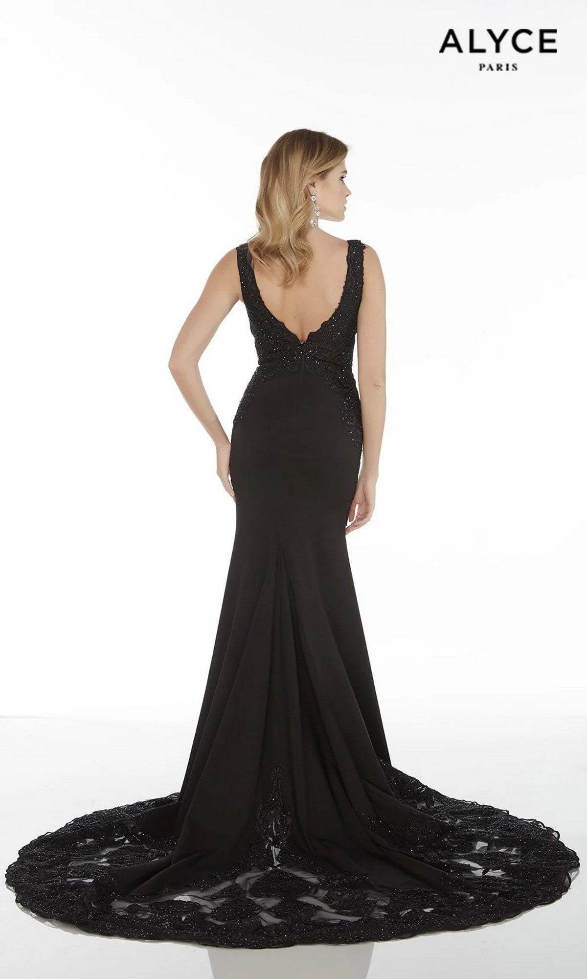 A woman wears the Alyce 5065 long formal dress, a sleeveless crepe gown featuring a deep V-back and embellished train, standing against a white background with the ALYCE Paris logo in the top right corner.
