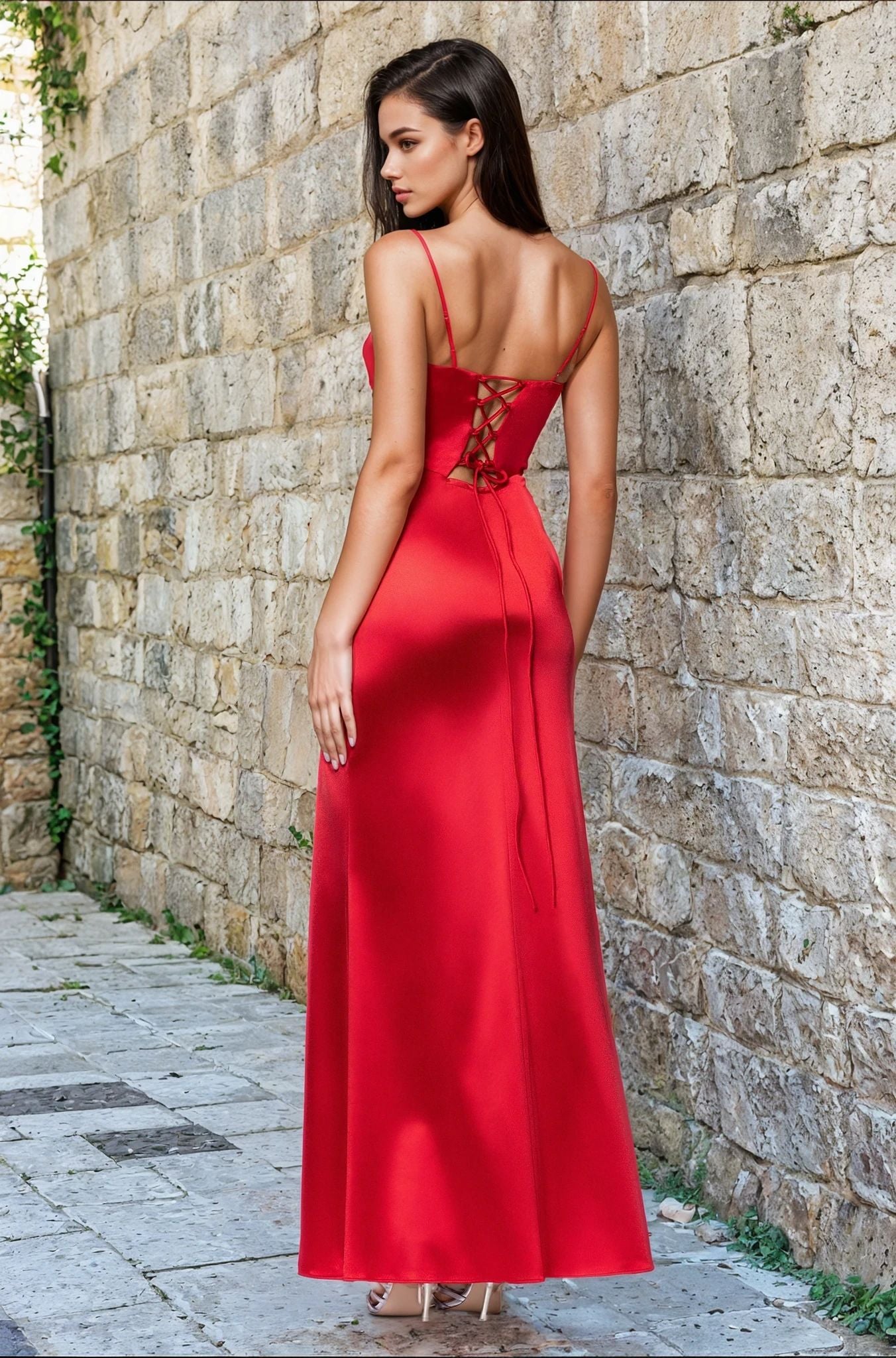 A woman wearing the Blondie Nites 5075BN Cut-Out Long Prom Dress with lace-up back stands on a stone walkway beside a textured stone wall.