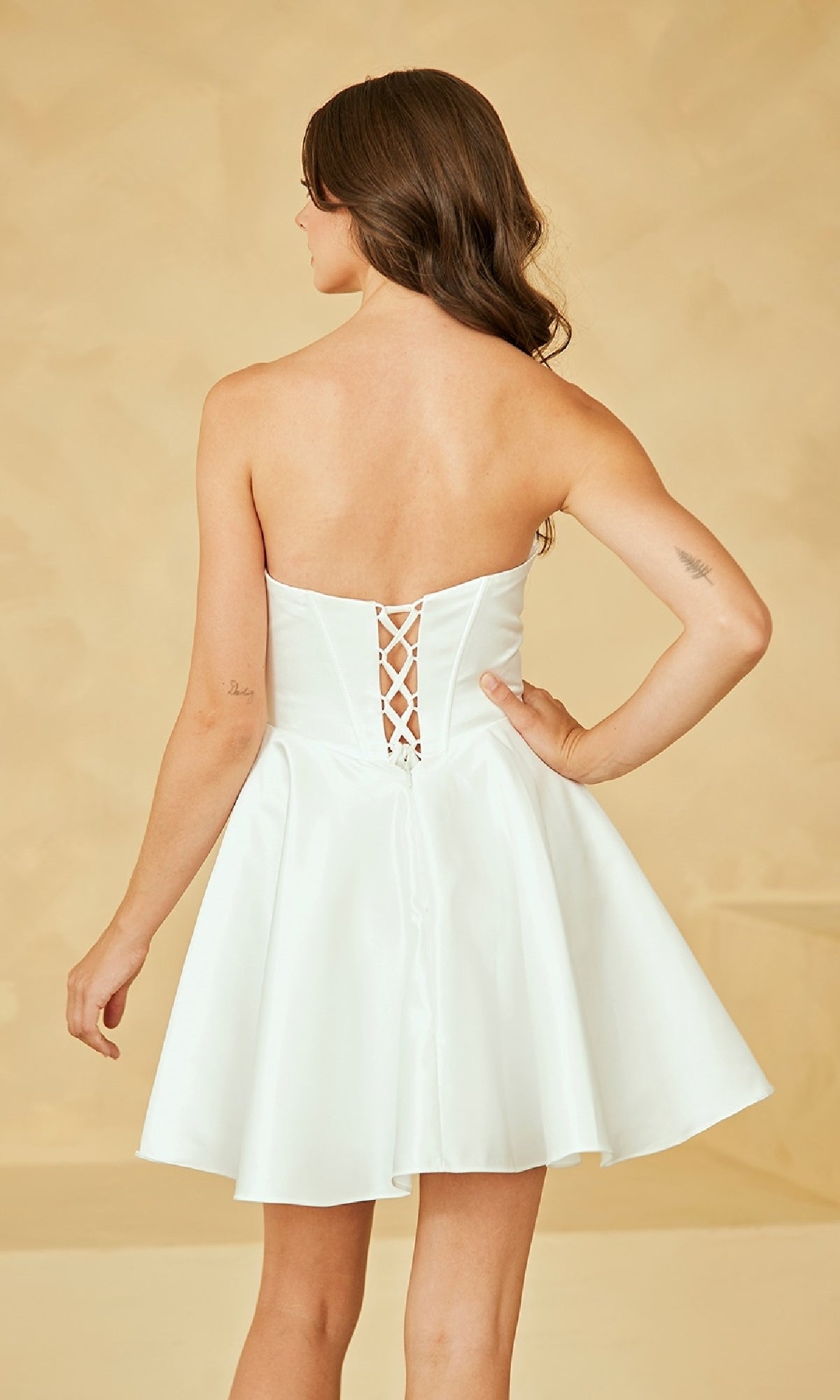 A woman stands facing away in the Amelia Couture 5082S strapless white party dress, showcasing its lace-up back, flared skirt, and corset-style bodice.