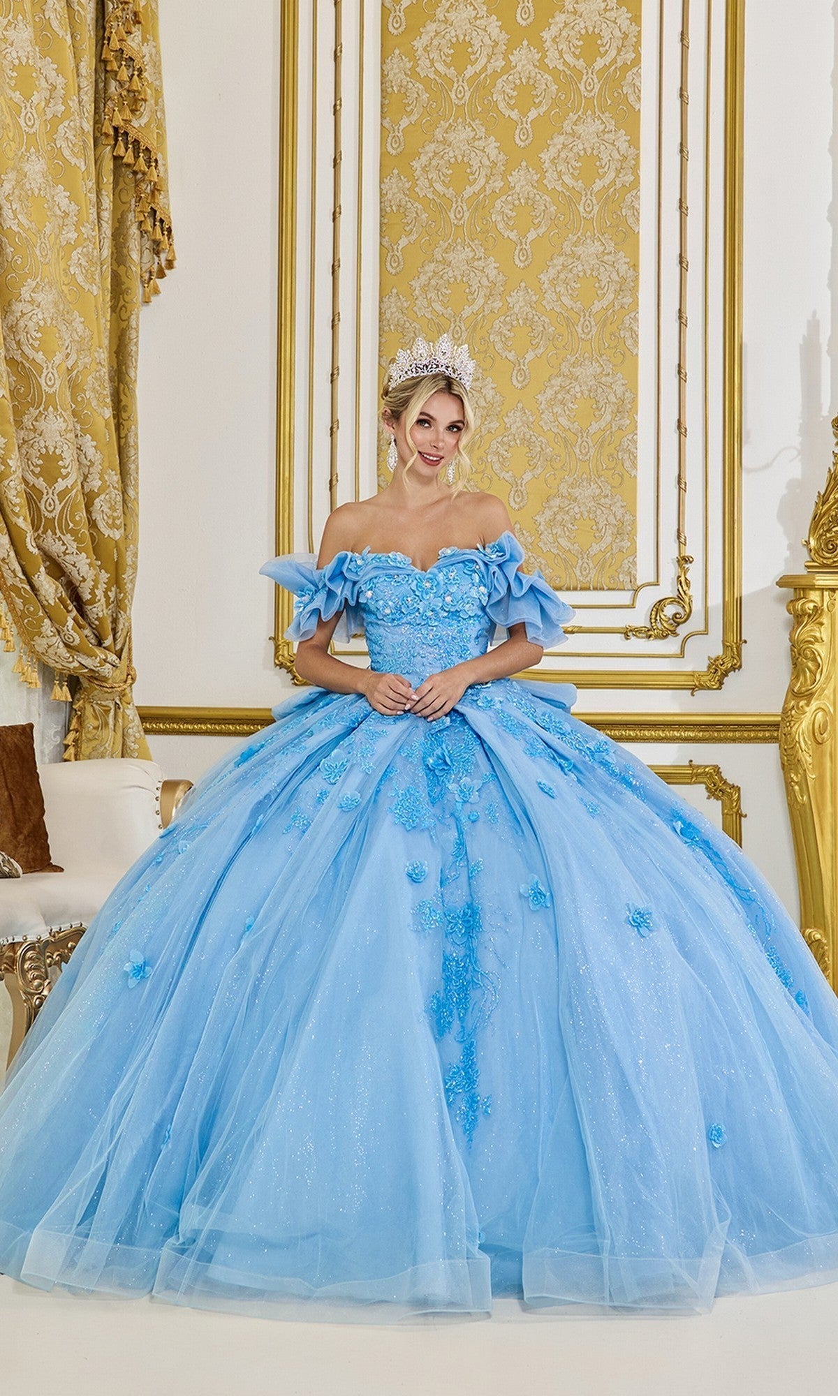 Wearing the Quinceanera Dress 5103 by Dancing Queen in Bahama Blue, a woman stands in an ornate gold and white room, smiling at the camera. The ballgown features a tulle skirt and delicate 3D floral appliques.