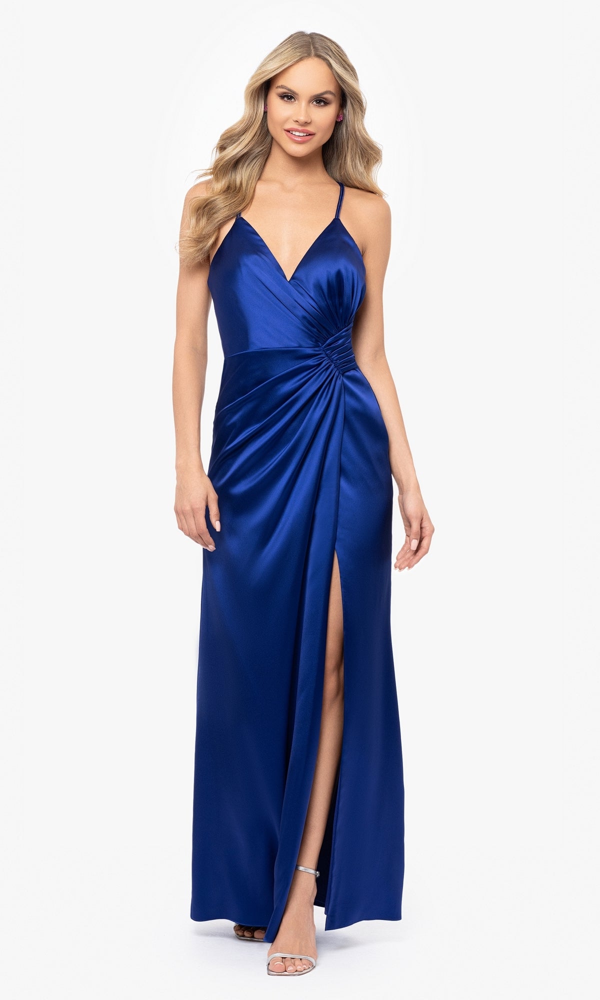 Model wearing the Blondie Nites 5119N, a sleeveless, floor-length royal blue stretch satin prom dress with spaghetti straps, ruched waist, and a front slit, posed against a white background.