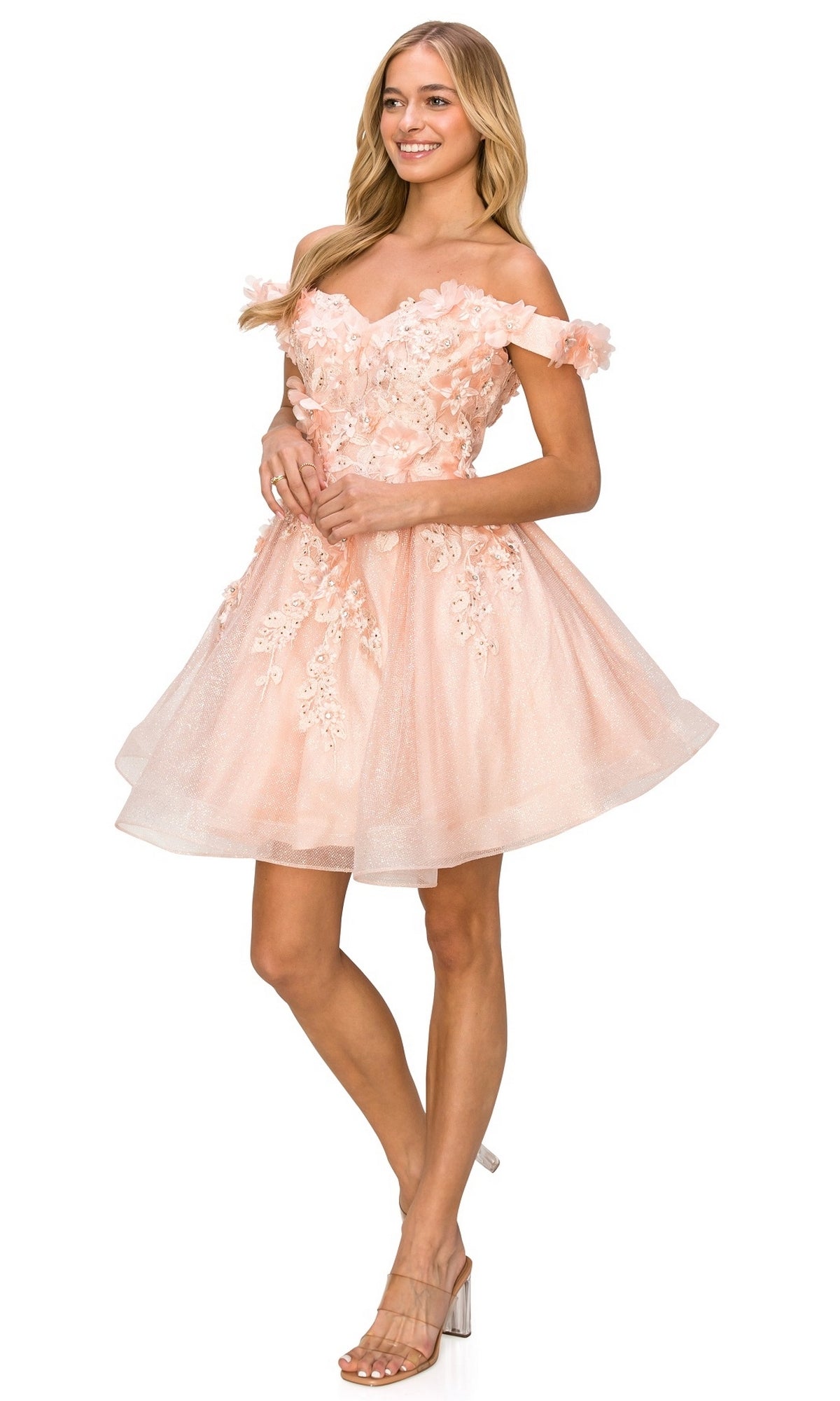 A woman in the Shimmer Off-Shoulder Short Homecoming Dress 5120J—a light pink, floral-detailed, sheer-layered baby doll party dress—styled with nude heeled sandals.