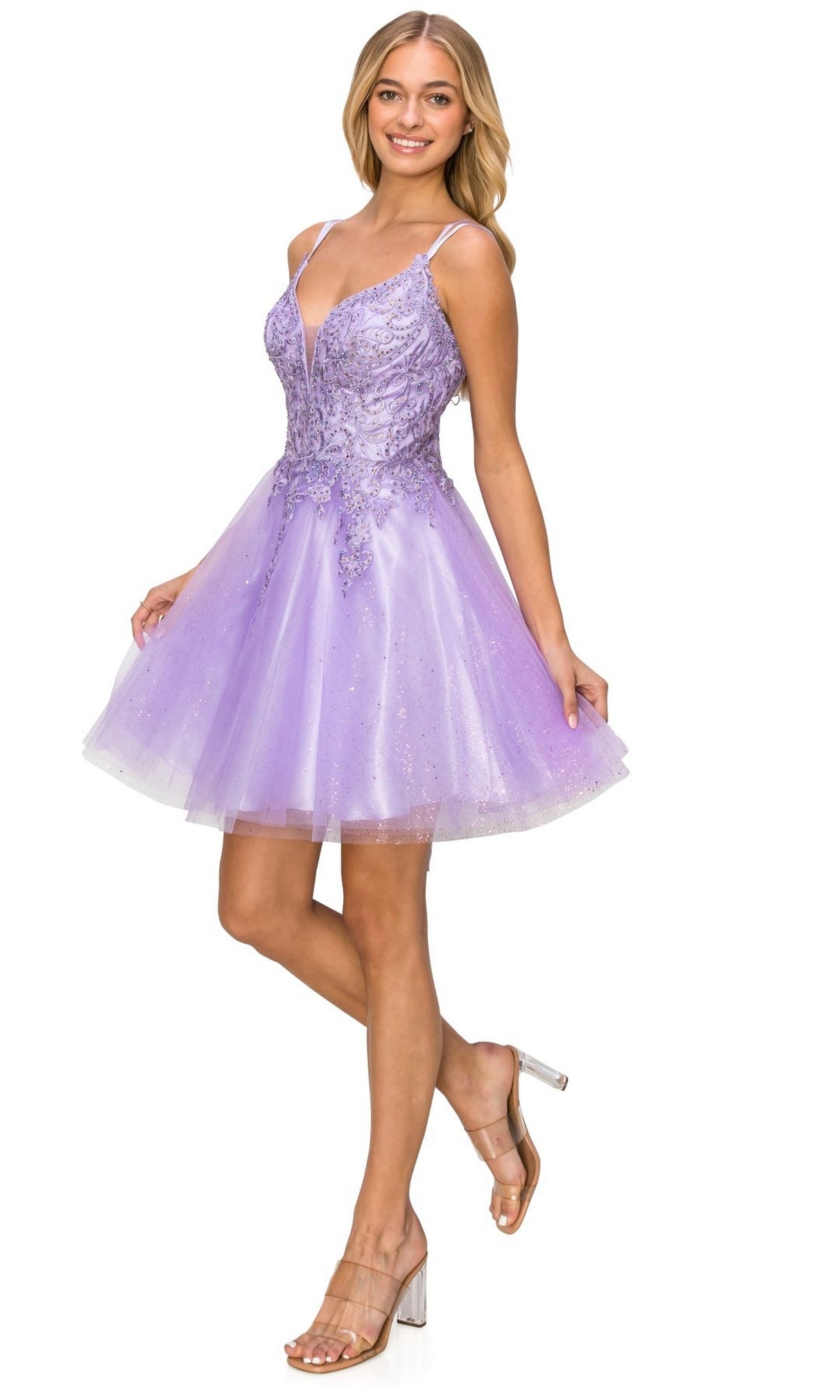 A woman poses in the Corset-Back Short Glitter Homecoming Dress 5125J, a sleeveless light purple A-line party dress with floral embellishments, paired with clear-strap heels against a white background.