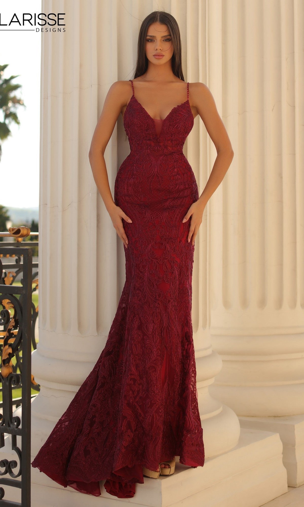 A woman stands before white columns wearing a fitted wine Long Prom Dress, Clarisse Designs 5138, featuring lace, thin straps, and a floor-length hem.