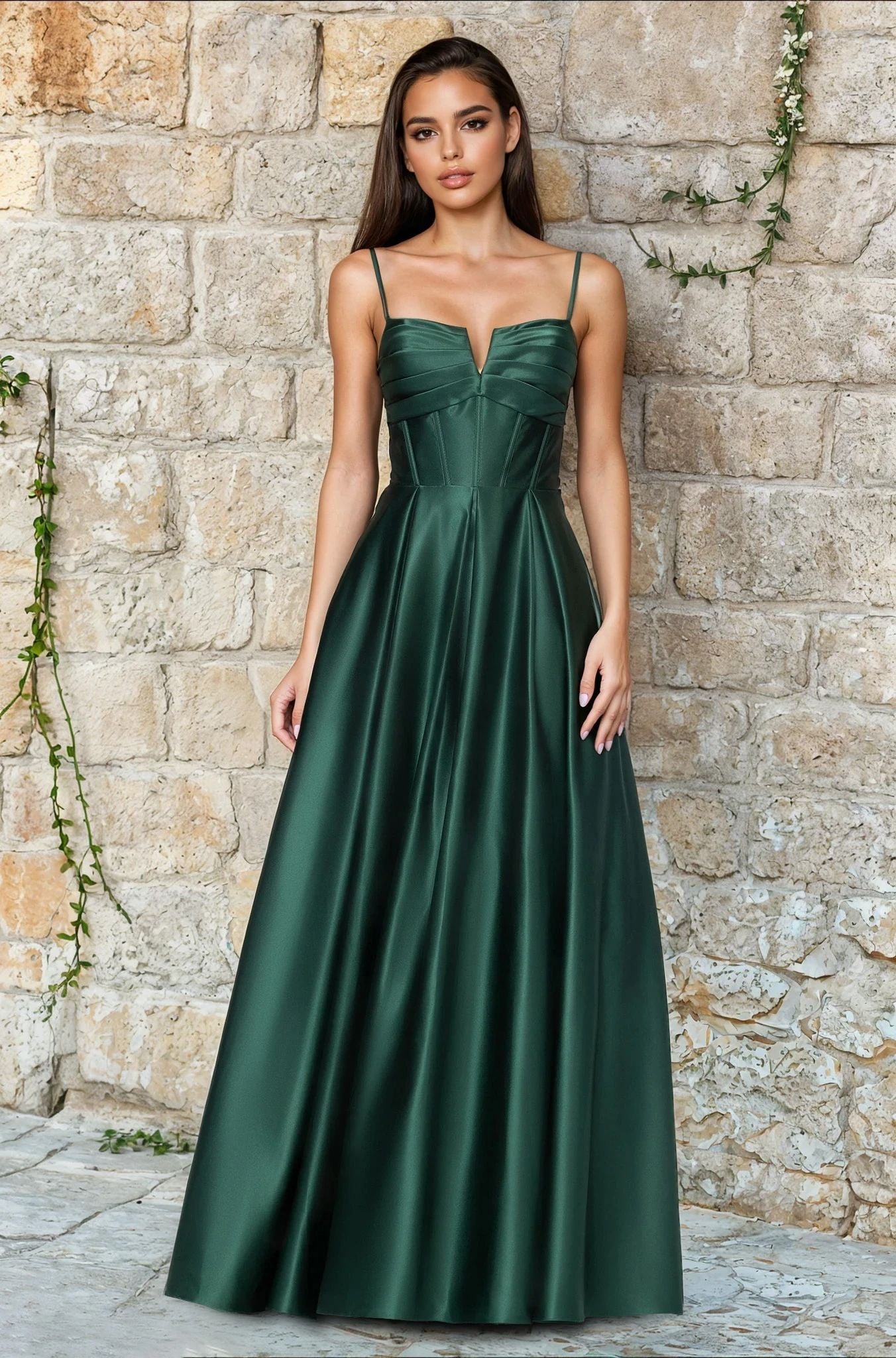 A woman poses by a stone wall in the Long Prom Dress: Blondie Nites 5207BN, featuring an elegant satin A-line silhouette with thin straps and a structured corset bodice—all for under $200.